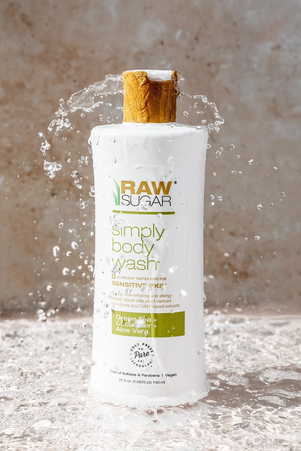A bottle of raw sugar body wash with a wooden cap, with water splashing around it.