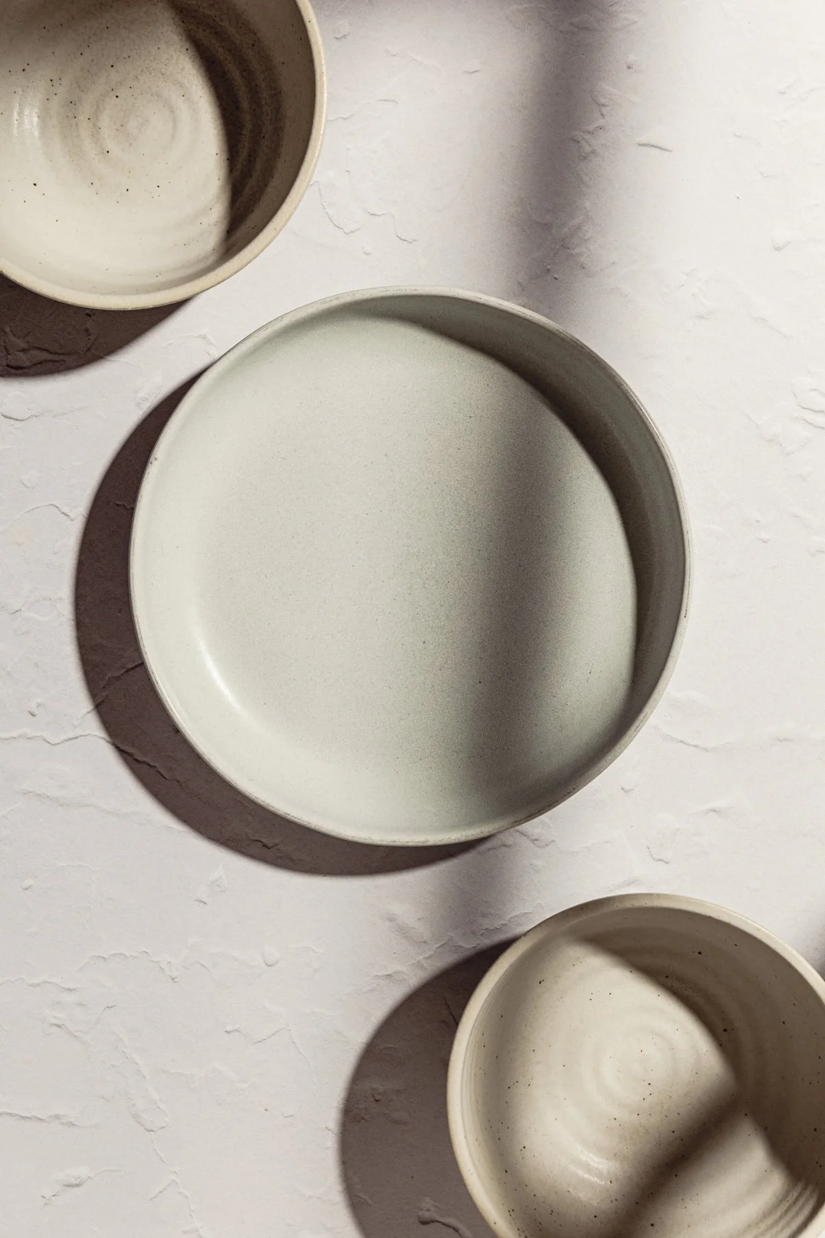 Three beige ceramic bowls placed on a textured white surface, with shadows cast to the left.