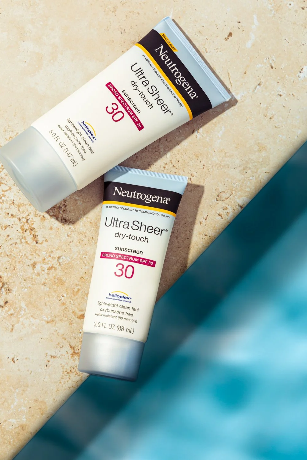 Two tubes of Neutrogena Ultra Sheer dry-touch sunscreen SPF 30 on a beige surface, with a blue cloth partially visible.