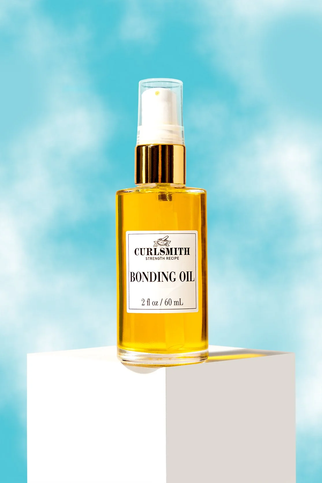 A bottle of Curlsmith Bonding Oil with a clear pump spray top and gold collar, sitting on a white pedestal against a bright blue sky background.