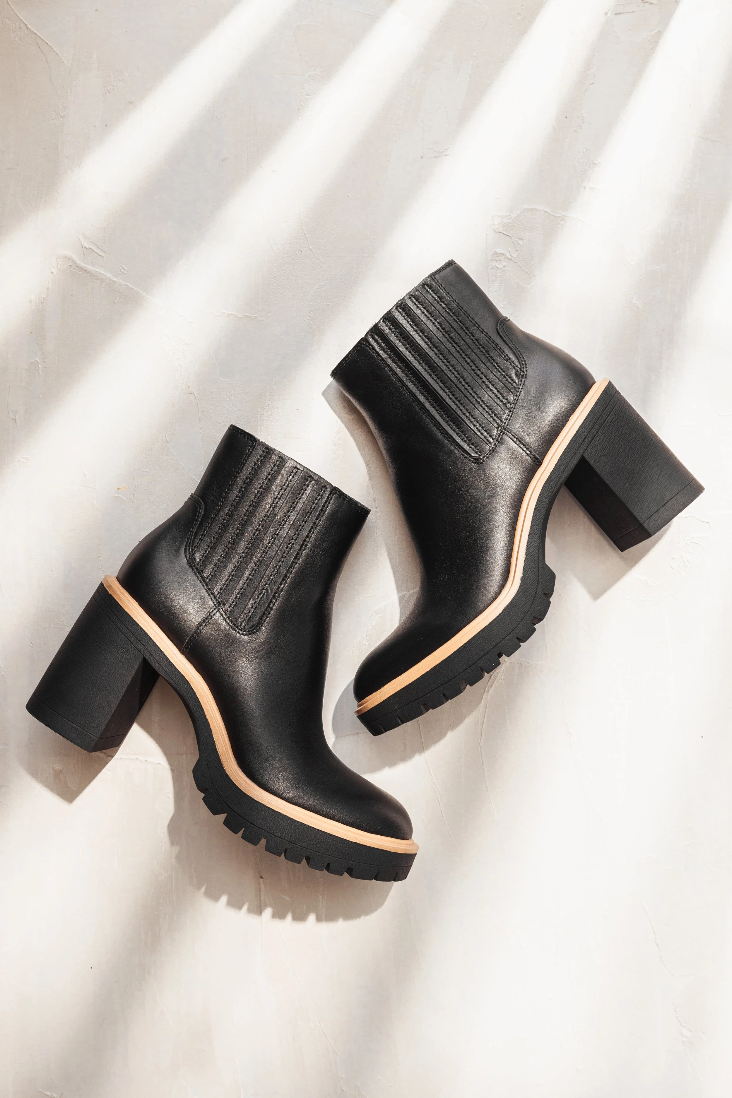 Pair of black leather ankle boots with chunky heels and beige soles on a white textured surface.