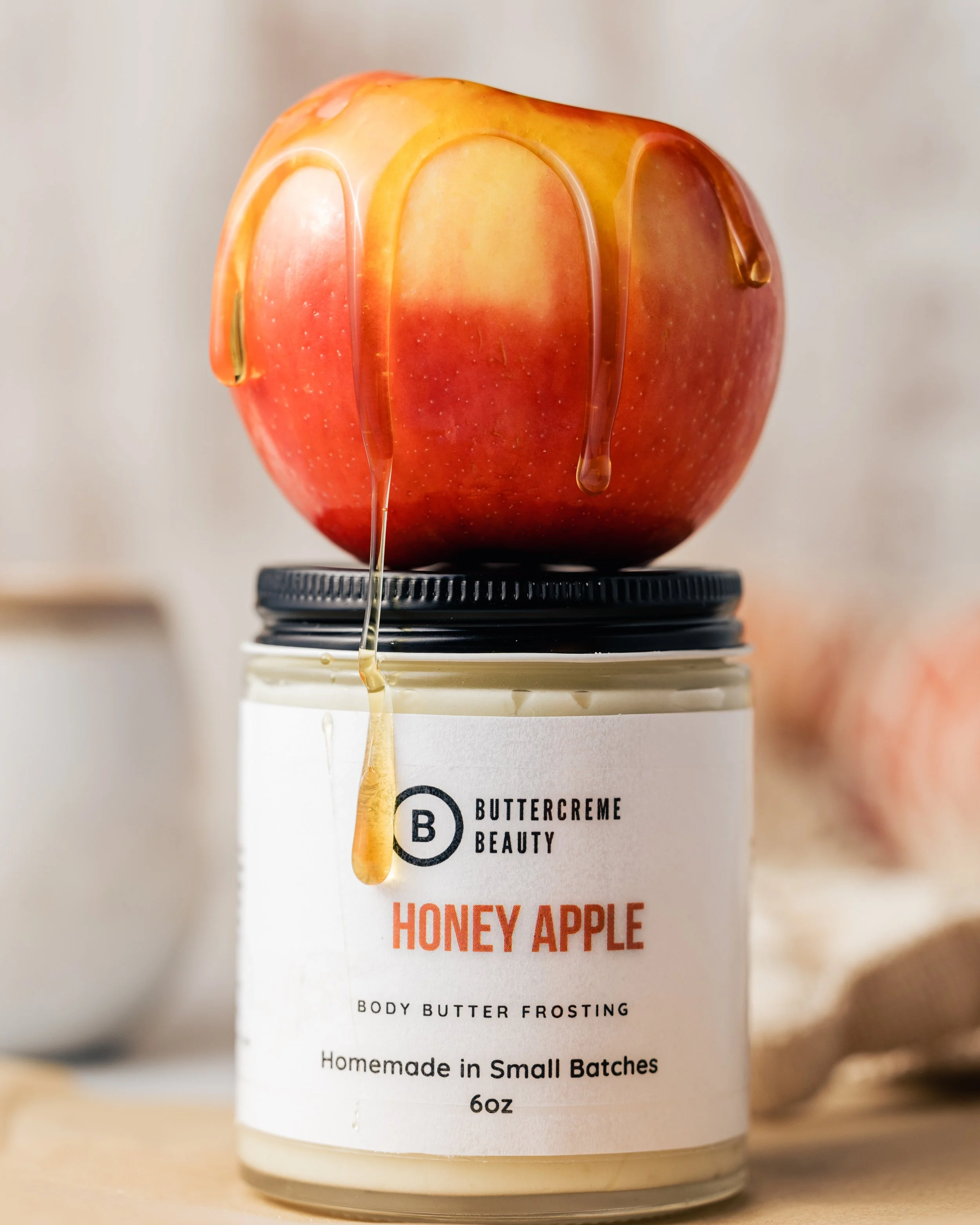 Red apple with honey drizzling over it, placed on top of a jar of Buttercreme Beauty Honey Apple body butter frosting.