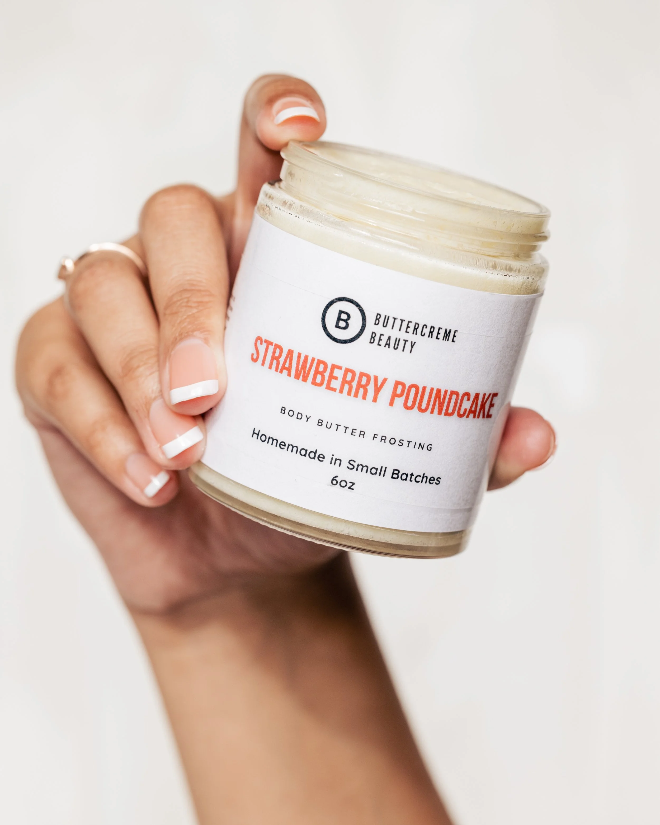 A person holding a jar of Buttercreme Beauty Strawberry Poundcake body butter frosting