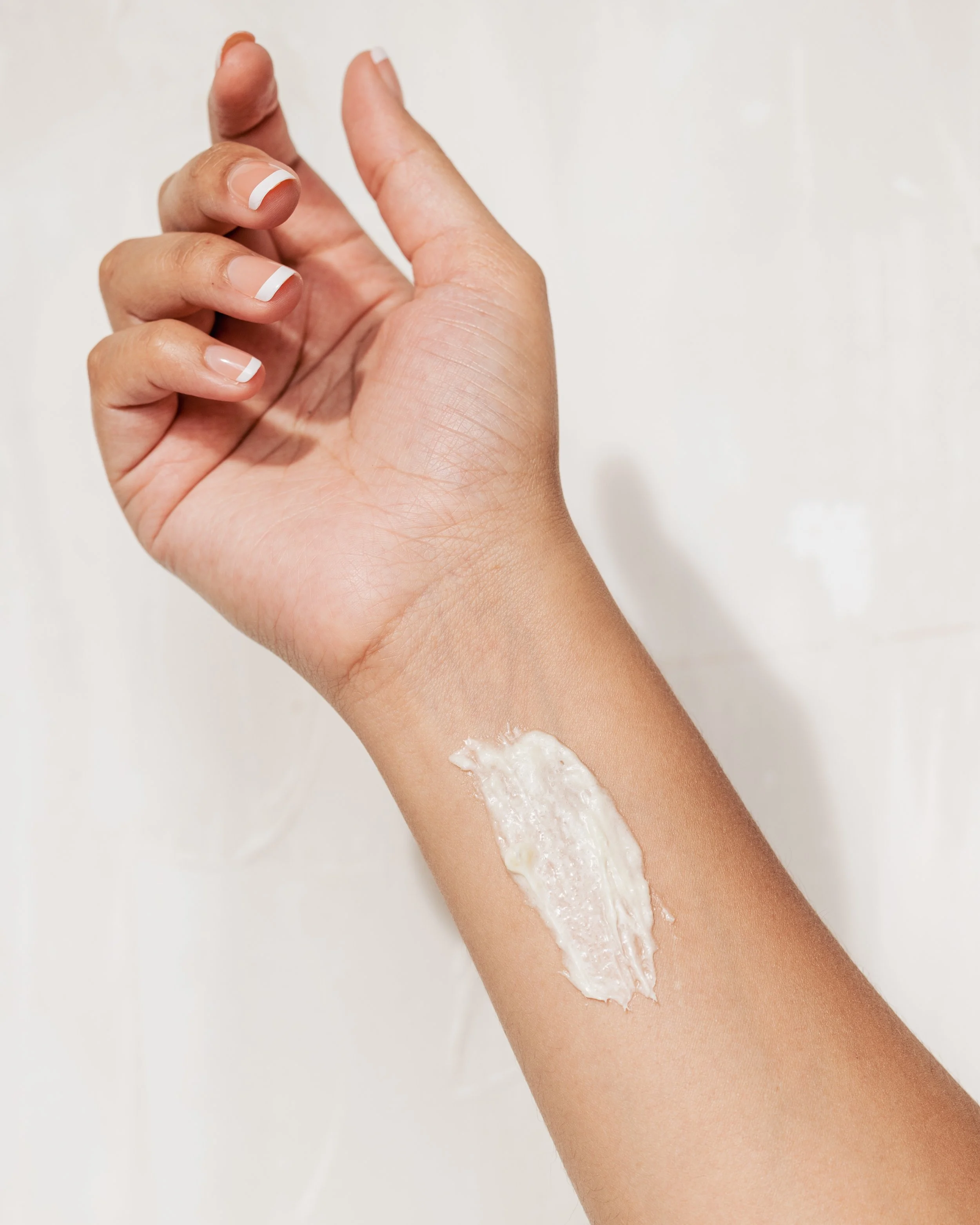 A person with medium skin tone applying lotion or cream to their forearm, with a patch of the product visible on the skin.