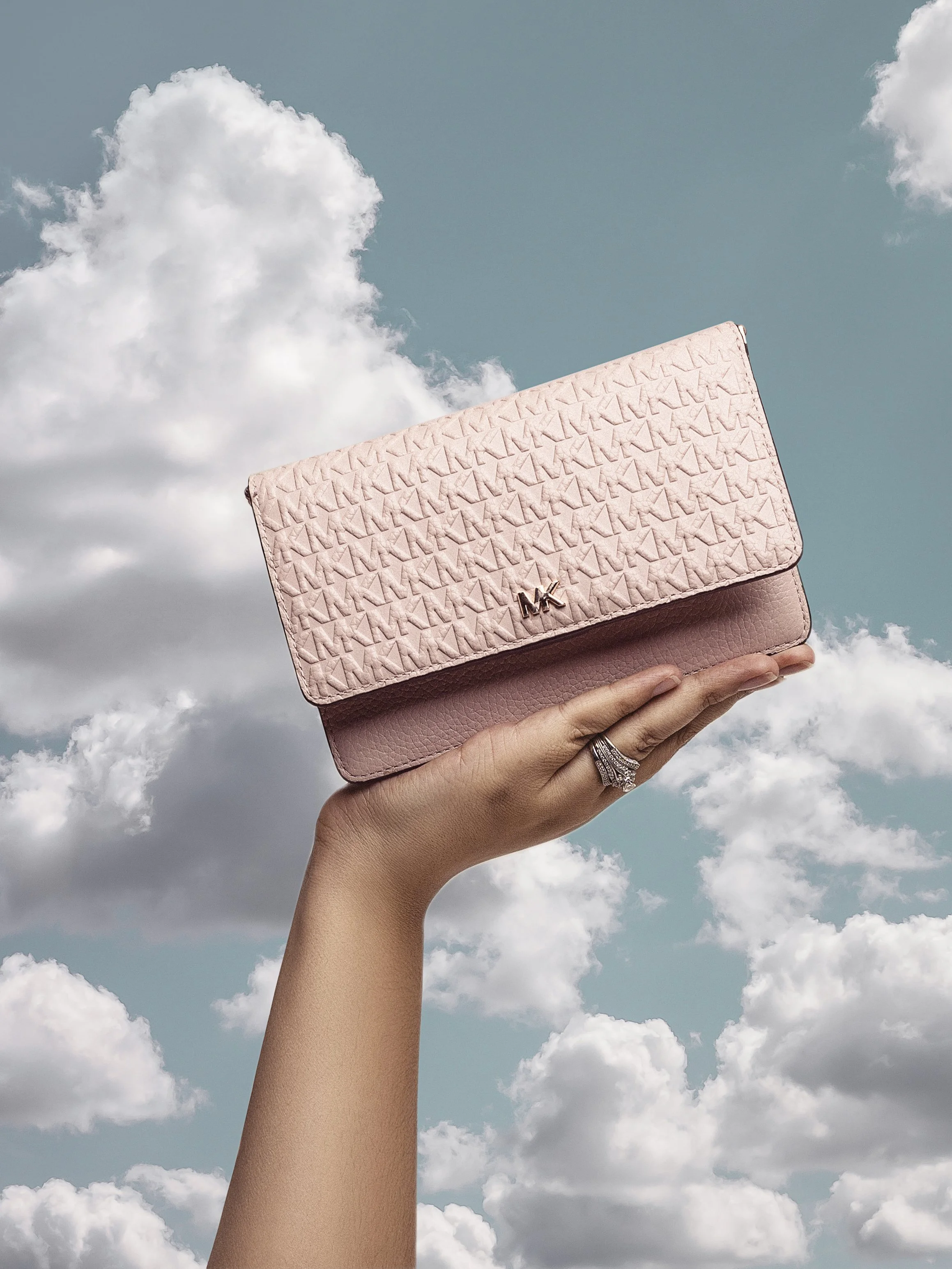 Hand holding up a pink Michael Kors wallet against a cloudy sky background.