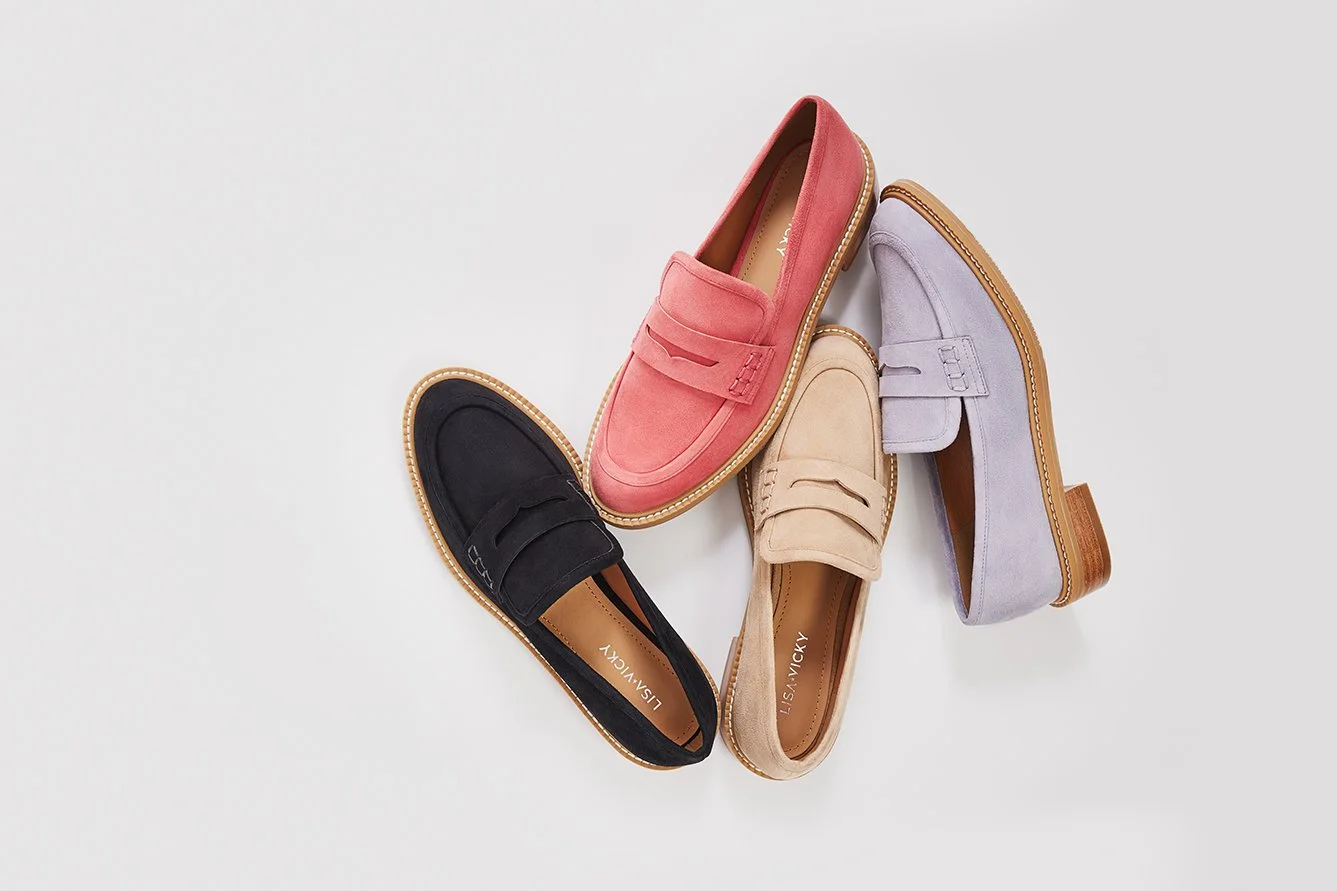 Four colored loafers (black, pink, beige, purple) with moccasin-style soles arranged on a white surface.