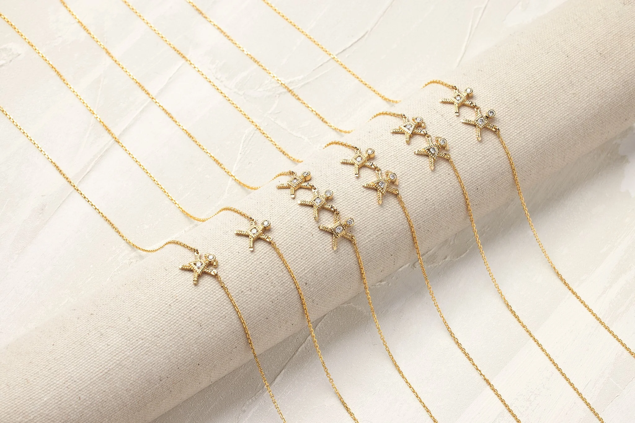 Multiple gold necklaces with star and sparkle charms displayed on a beige fabric surface.