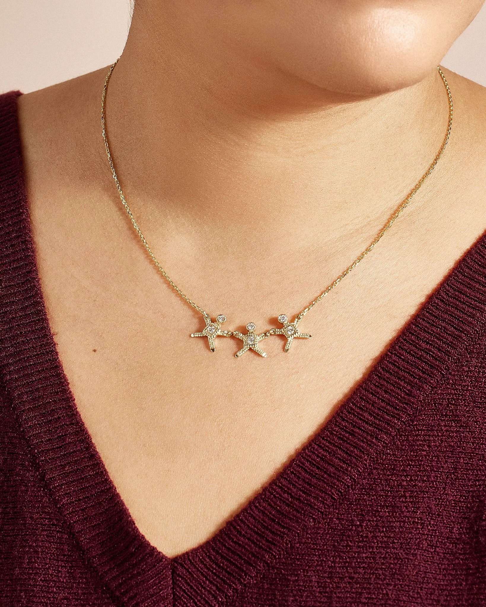 Close-up of a person's neck wearing a gold necklace with three star-shaped charms adorned with small gemstones.