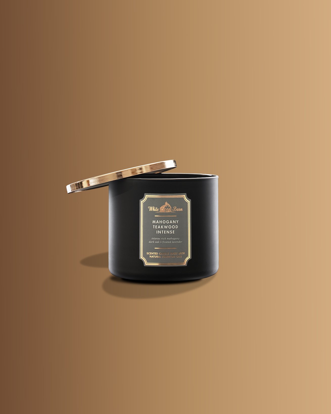 A black candle jar with a gold lid, labeled as Mahogany Teakwood Intense scented candle by White Barn, against a brown background.