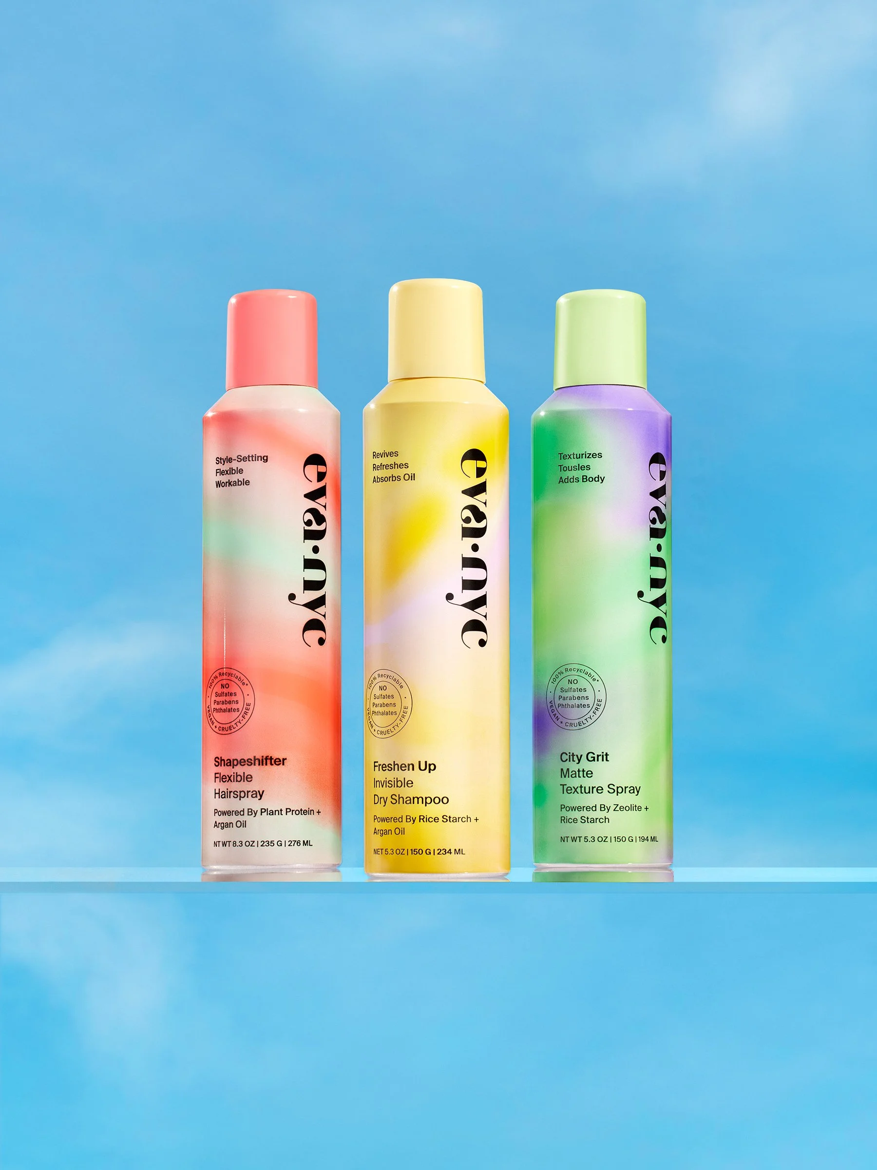 Three hair spray bottles with colorful gradient designs on a glass surface against a blue sky background.