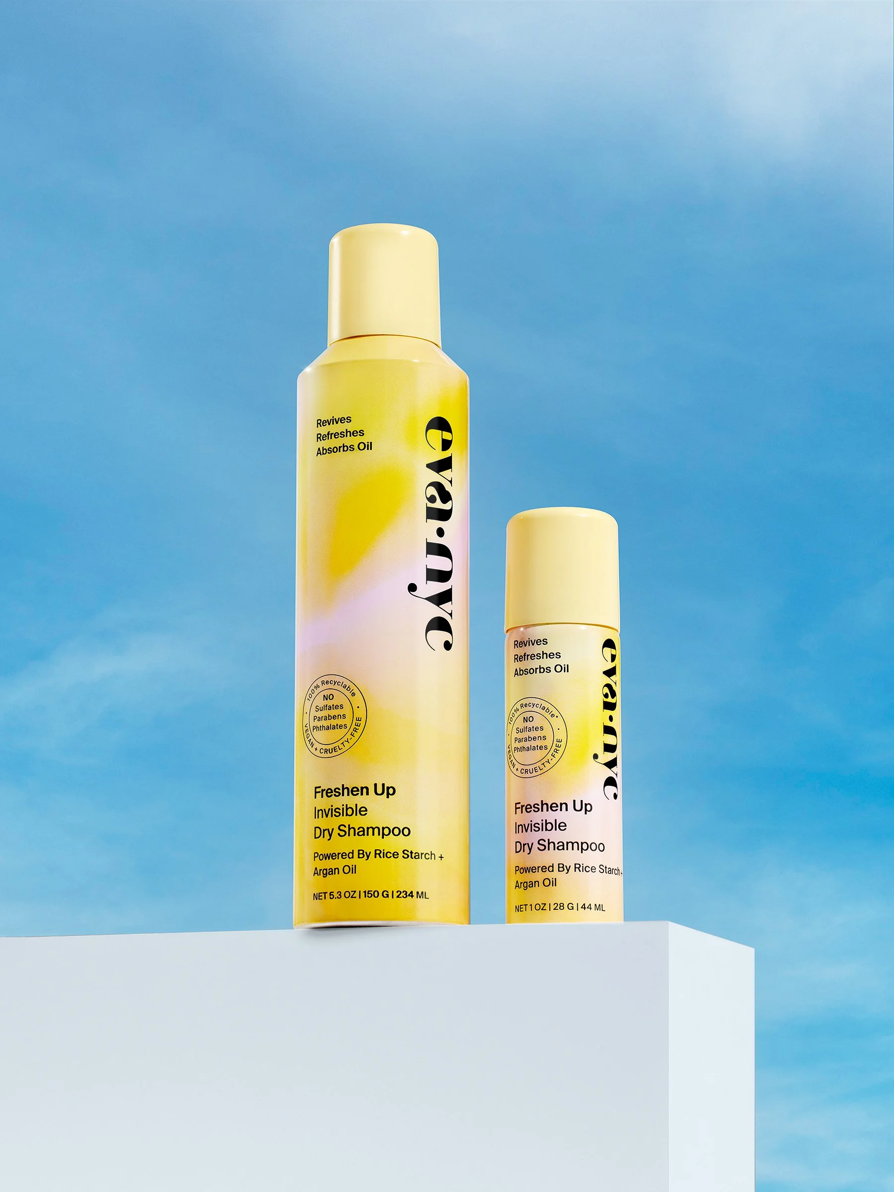 Two bottles of Eva NYC Freshen Up Invisible Dry Shampoo, one large and one small, placed on a white surface against a blue sky background.