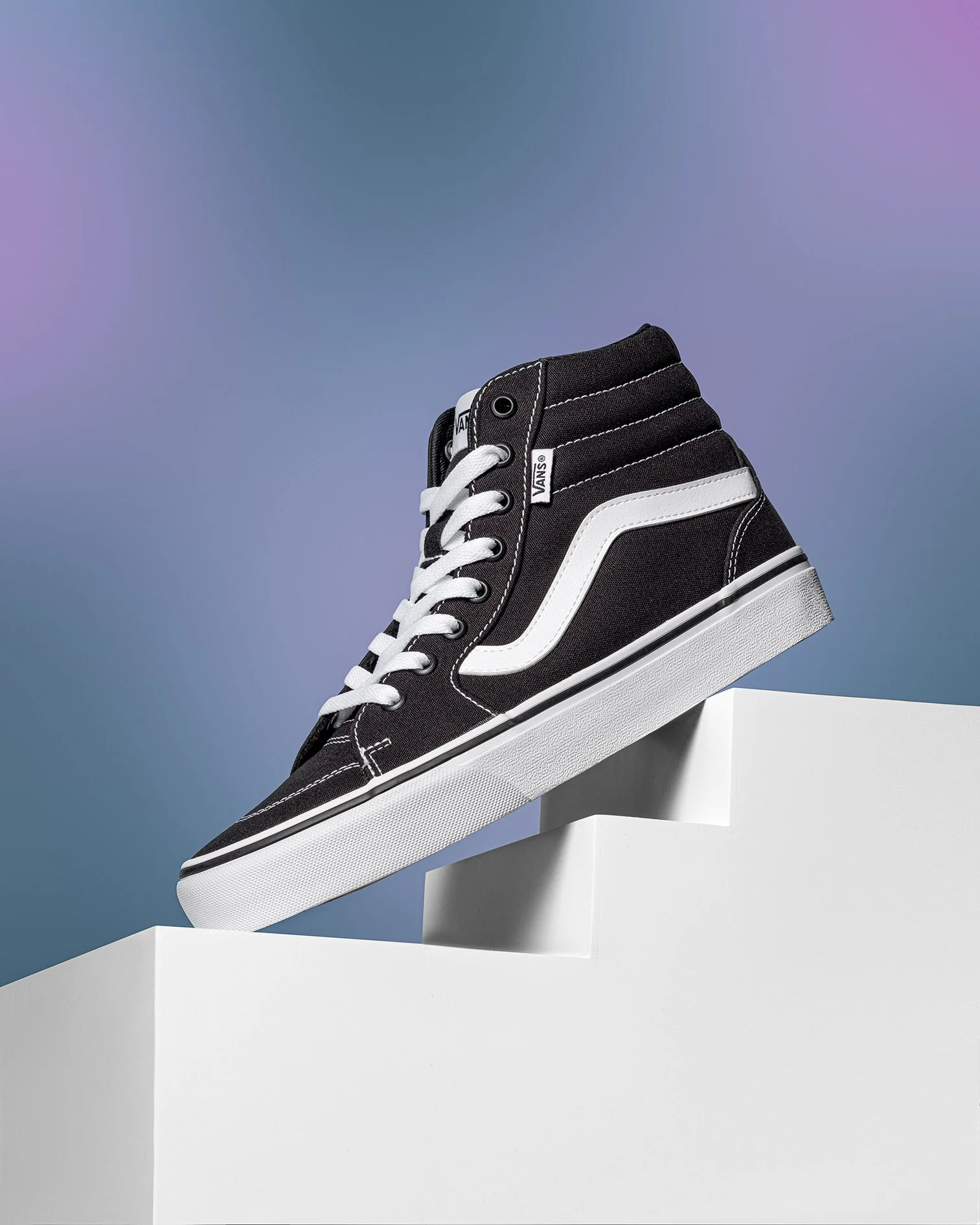 A black and white Vans high-top sneaker displayed on a white stand against a blue gradient background.