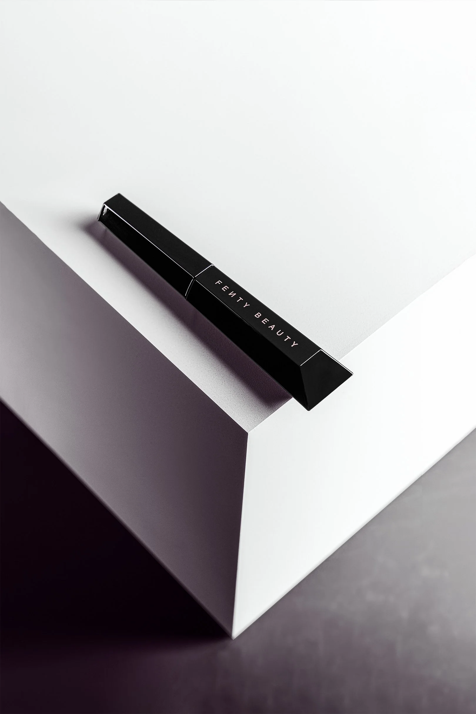 A black lipstick tube with the brand name 'Fenty Beauty' lying on a white surface with a dark background.