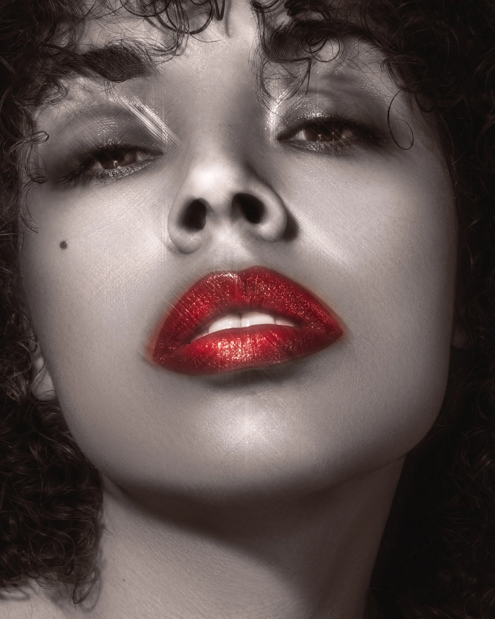 Close-up of a woman's face with curly hair, red lipstick, and eye makeup, in black and white