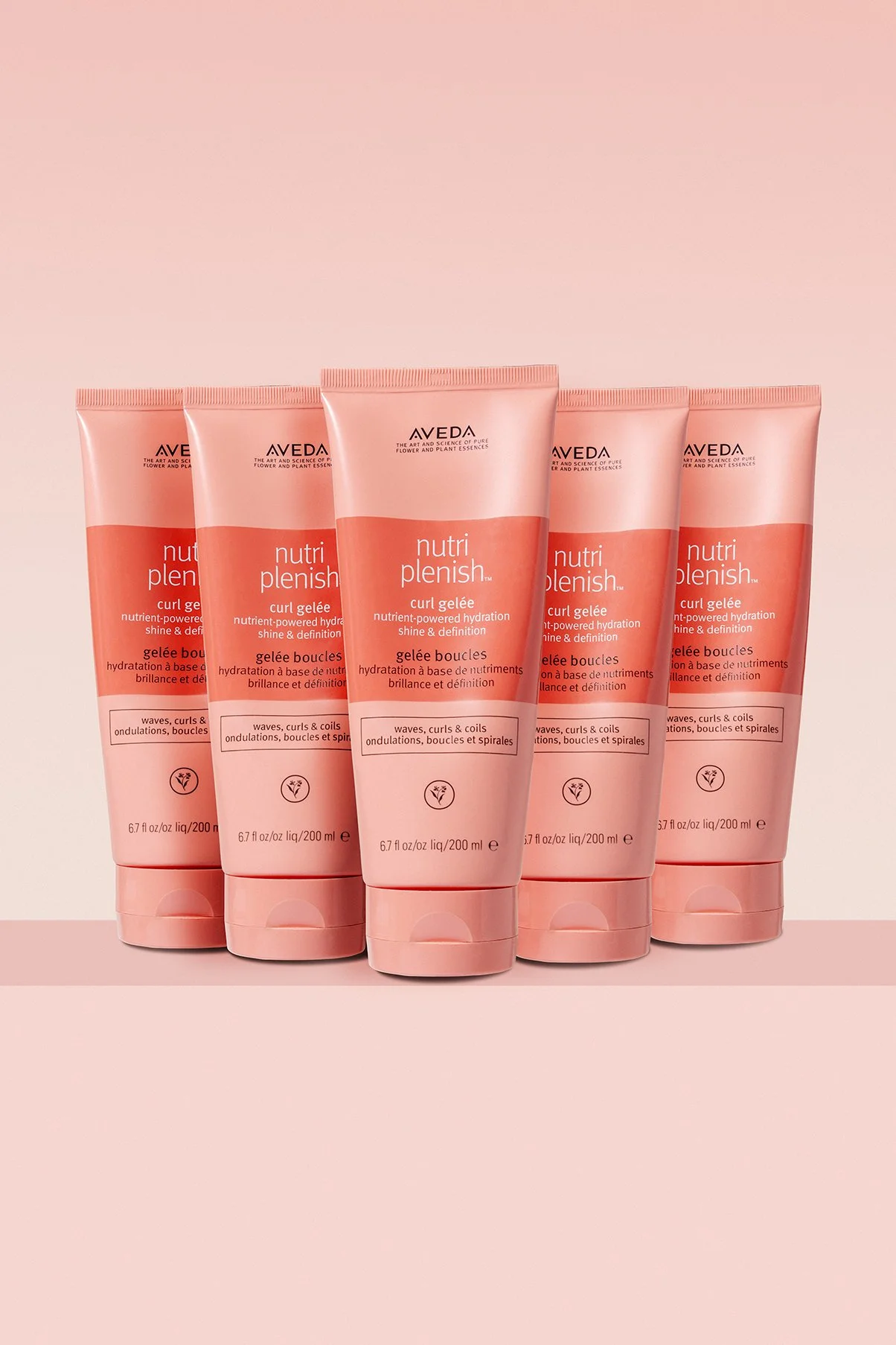 Five bottles of Aveda Nutri Plenish Curl Gelée hair product lined up against a pink background.