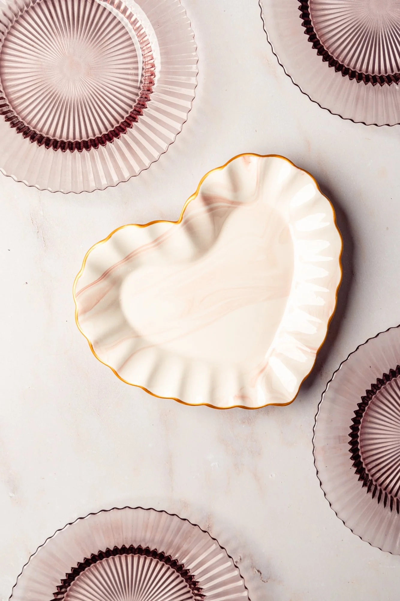 Decorative ceramic dishes in pink and white with gold accents, arranged on a light-colored surface.