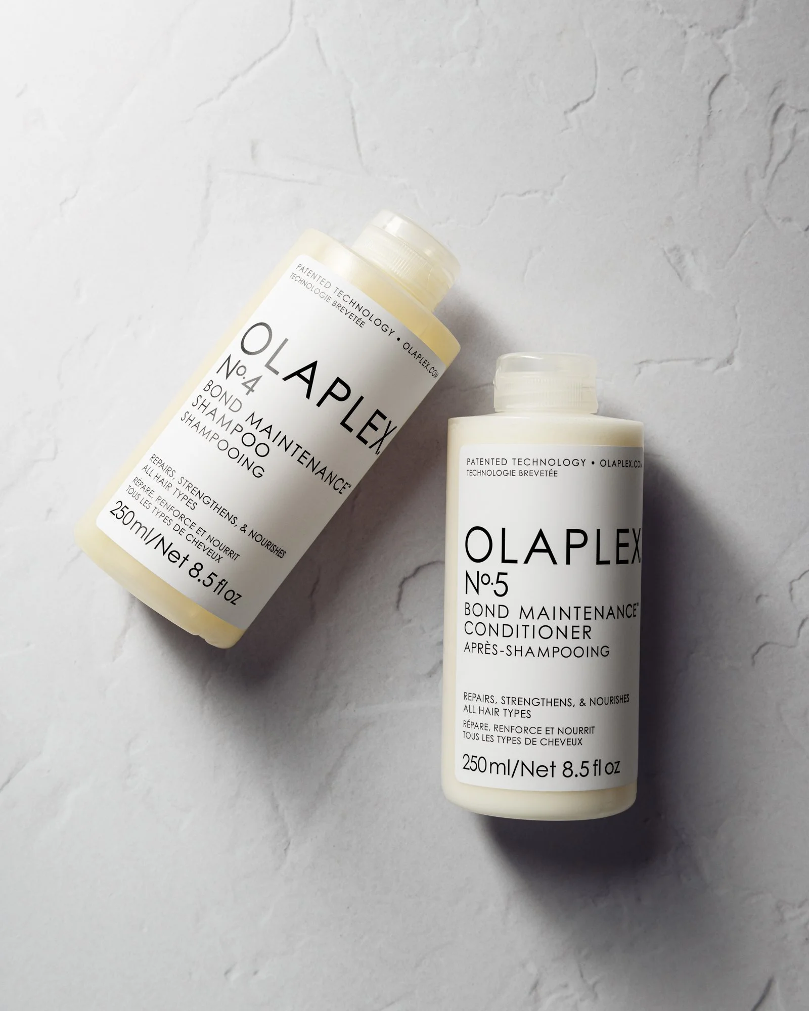 Two bottles of Olaplex hair care products, Bond Maintenance Shampoo No.4 and Bond Maintenance Conditioner No.5, on a light textured surface.