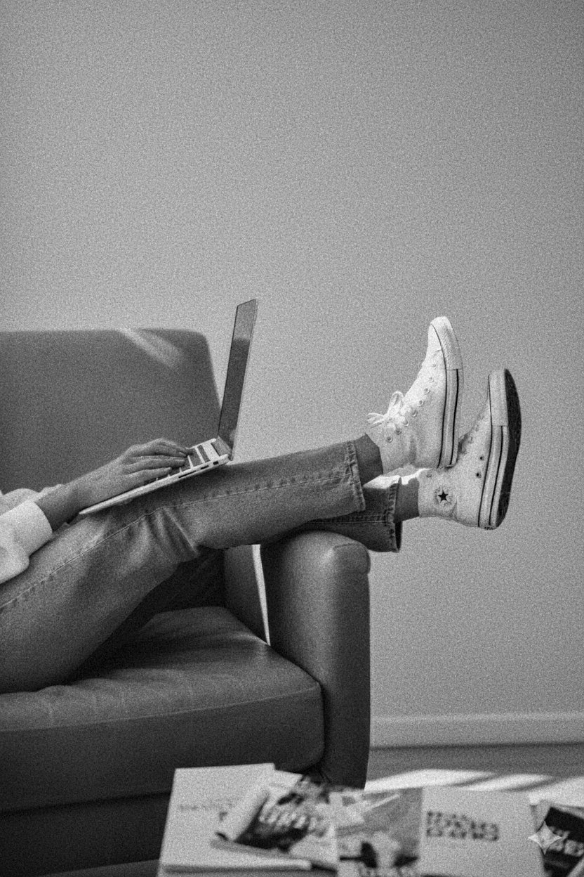 woman's legs hanging off the side of a couch with converse shoes working on a laptop