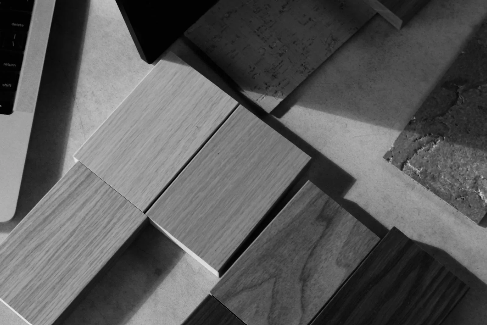 Top-down view of several wooden sample panels with different grain and finish, positioned on a concrete surface next to a laptop keyboard in the upper left corner.