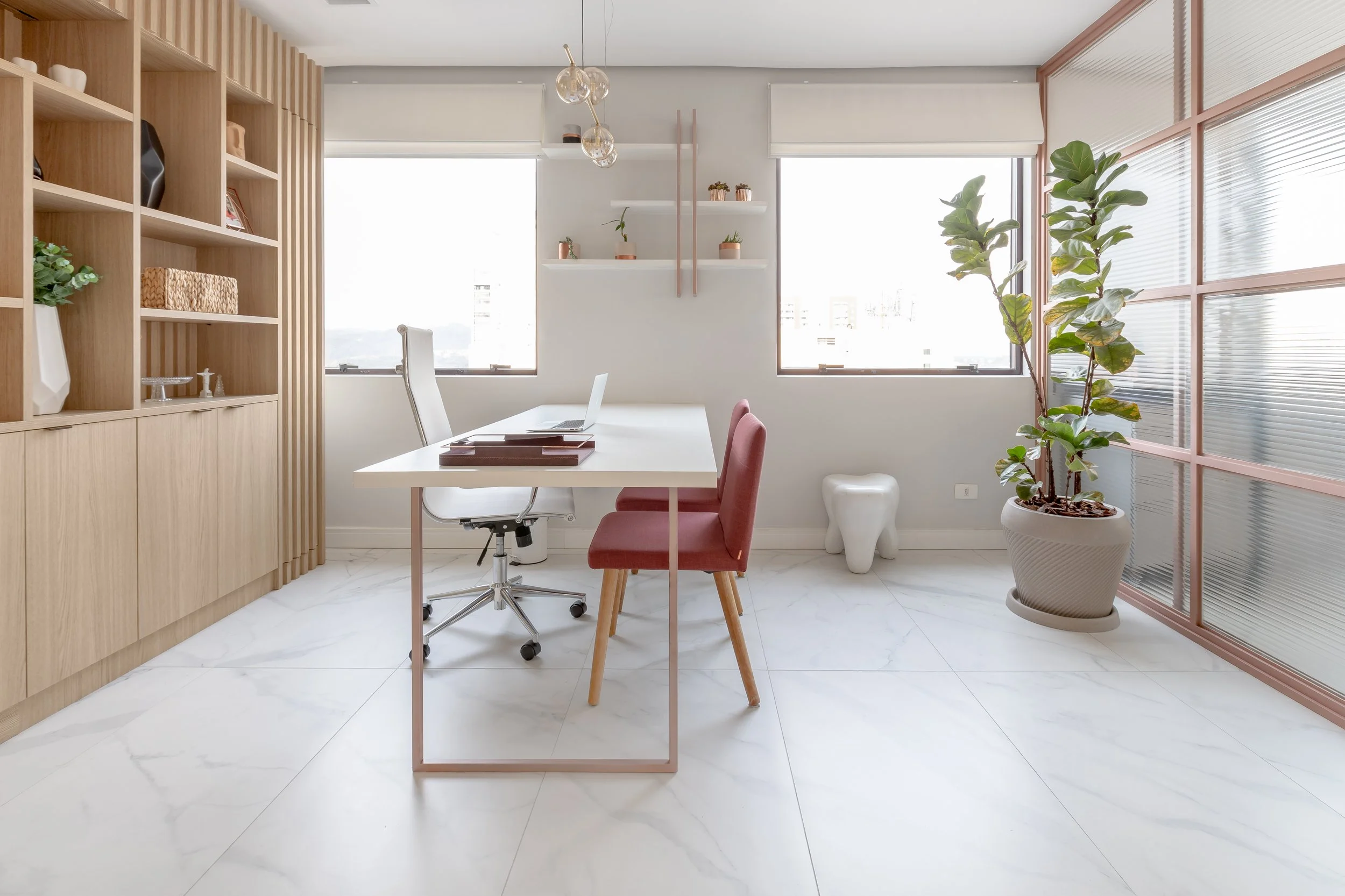 Escritório moderno com mesa branca, cadeira rosa, cadeira branca de escritório, estantes de madeira, plantas em vasos, janelas grandes, piso de mármore branco e decoração minimalista.
