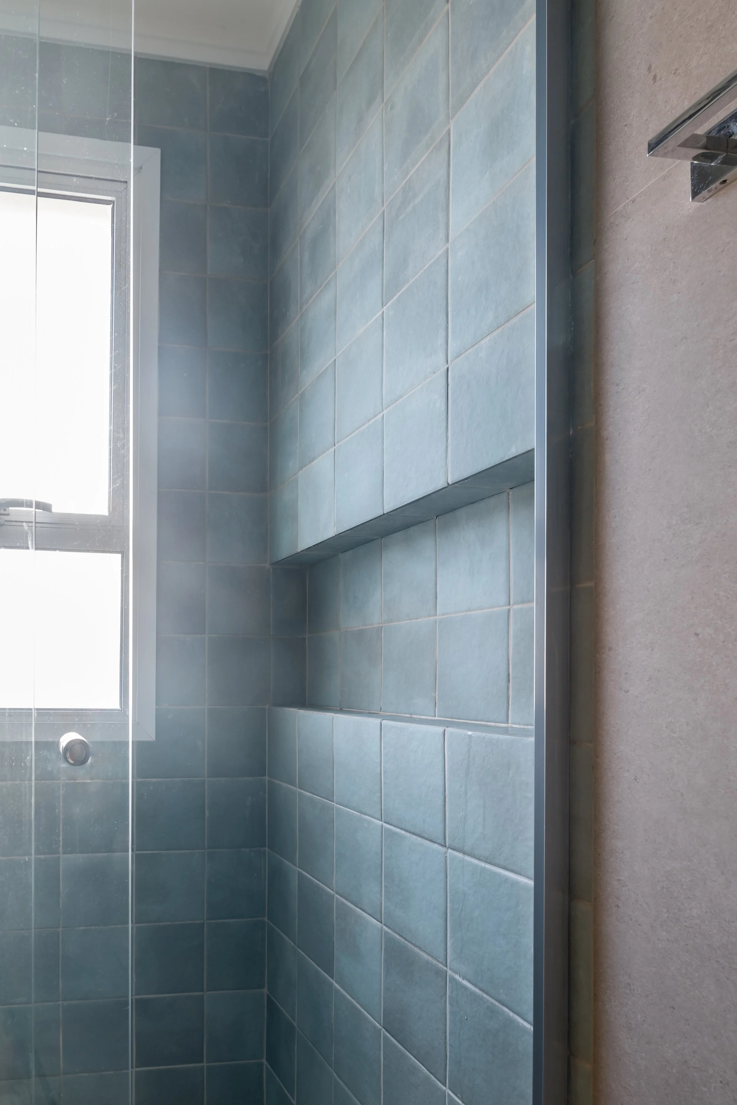 Interior de um banheiro com paredes revestidas de azulejos azuis e uma janela de vidro na parede do fundo.