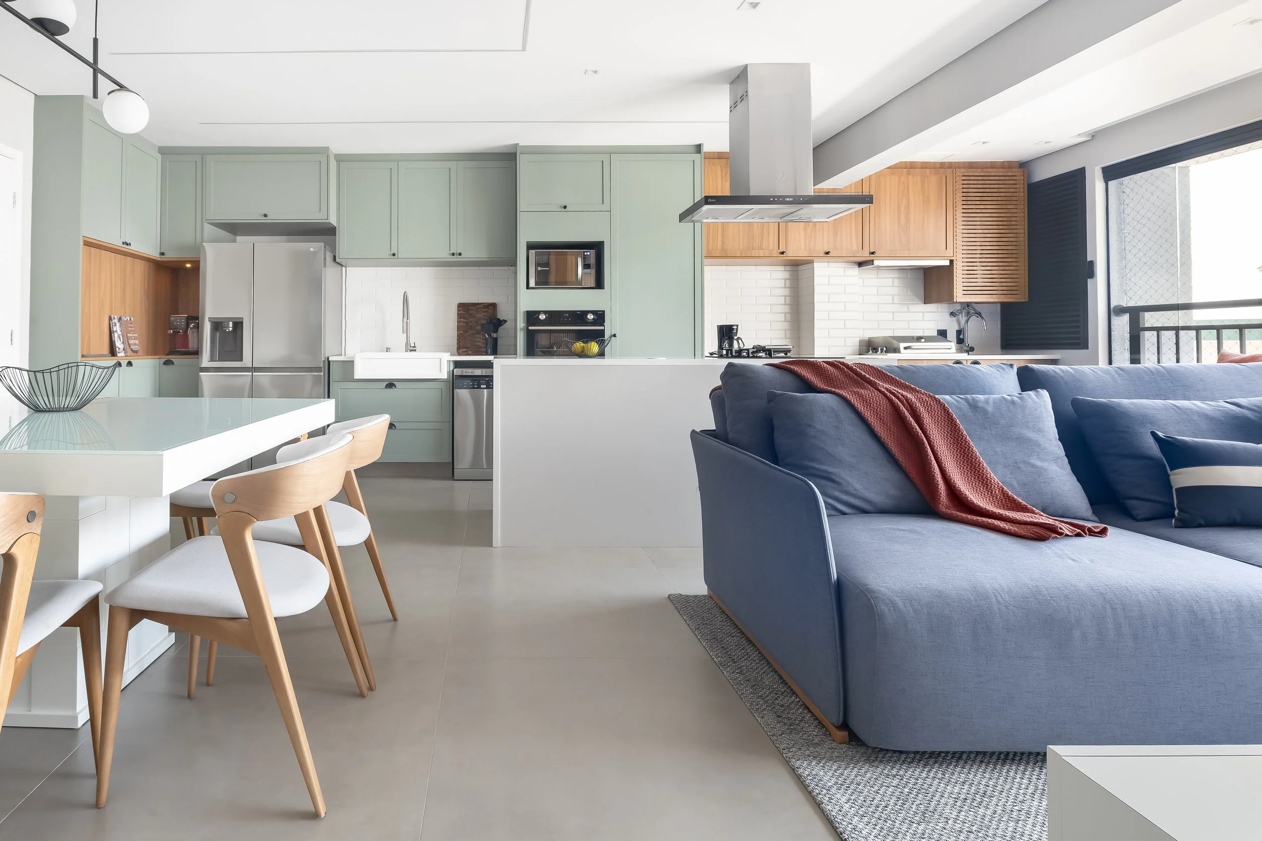 Sala de estar integrada à cozinha com móveis de cores suaves e janelas com cortinas pretas