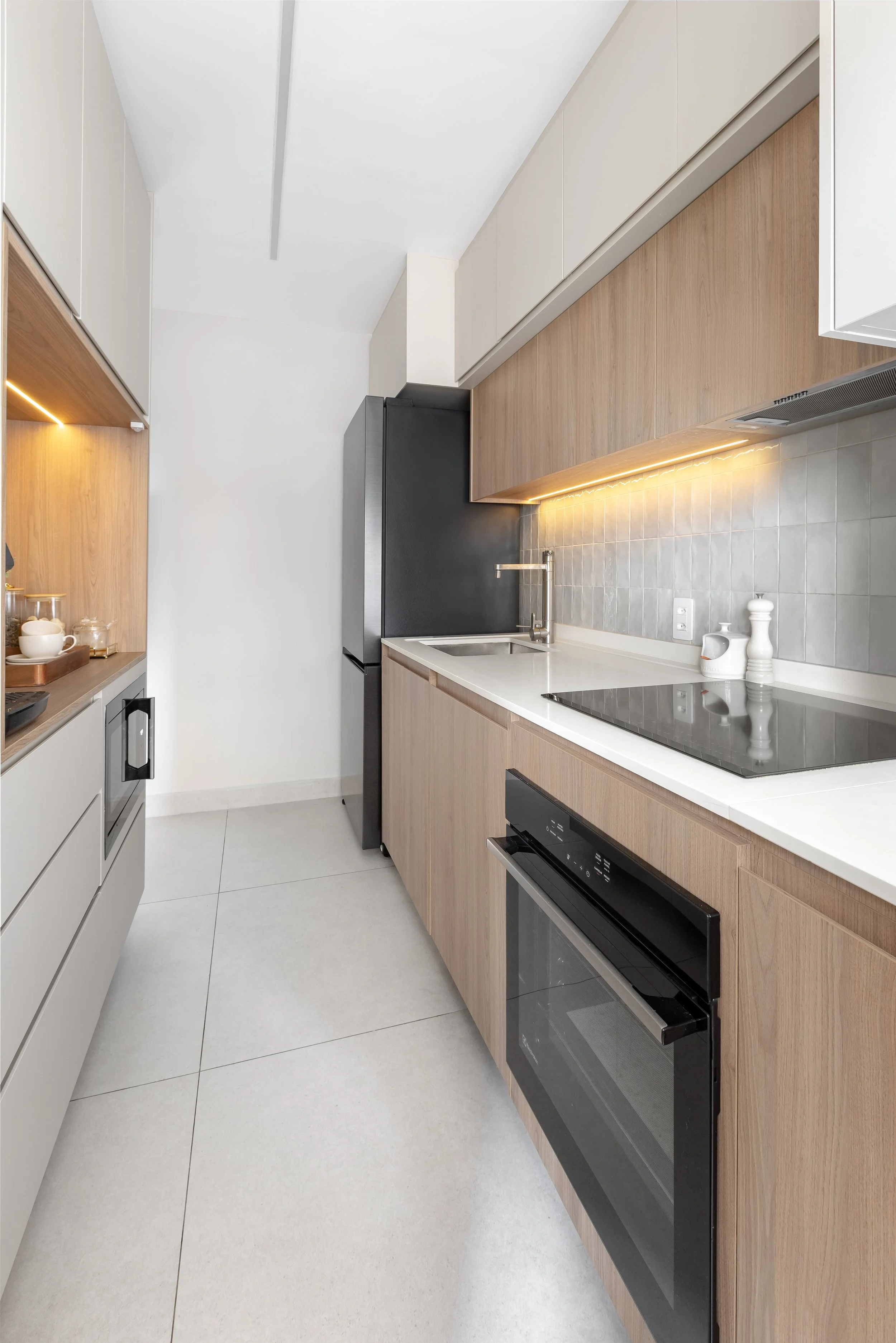 Cozinha moderna com armários claros, bancada de mármore, pia de aço inox e eletrodomésticos em aço escovado, incluindo geladeira e forno, com iluminação sutil