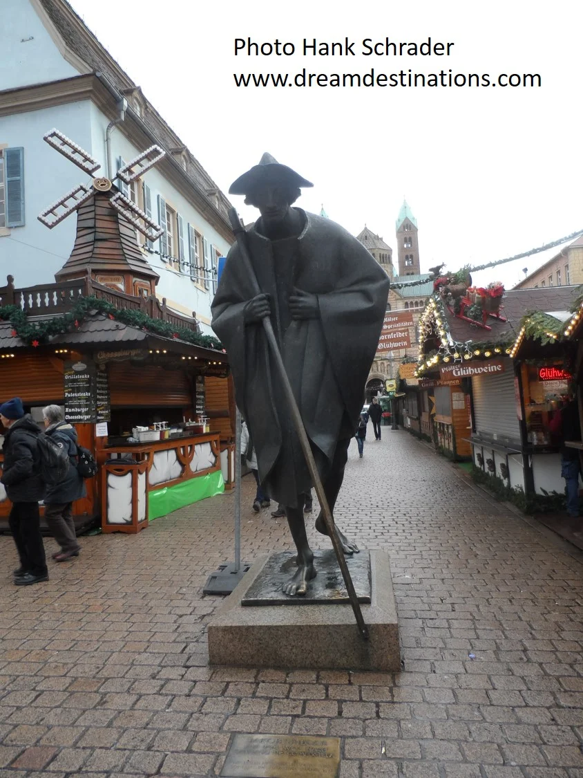 Speyer Germany Christmas Markets. In the foreground is a statue of a pilgrim on the way to Santiago de Compostela, with the Cathedral in the background. Speyer was an important stop on this pilgrimage route.
