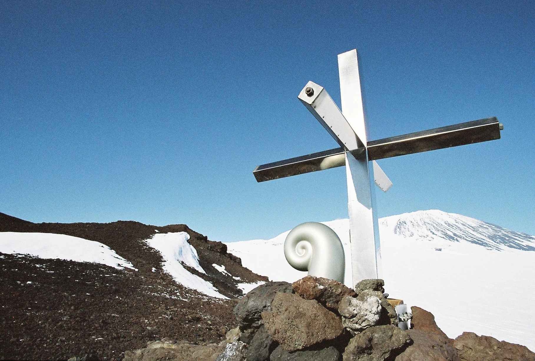 Koru capsule and cross on Mt Erebus. The cross is located approximately 3 km south-east of the 1979 crash site. This stainless steel cross was erected in 1987 to replace the original wooden one, which had eroded. The Koru was created by Christchurch sculptor, Phil Price. Photo credit: Daniel O’Sullivan, 2009-10, Antarctica New Zealand Pictorial Collection.