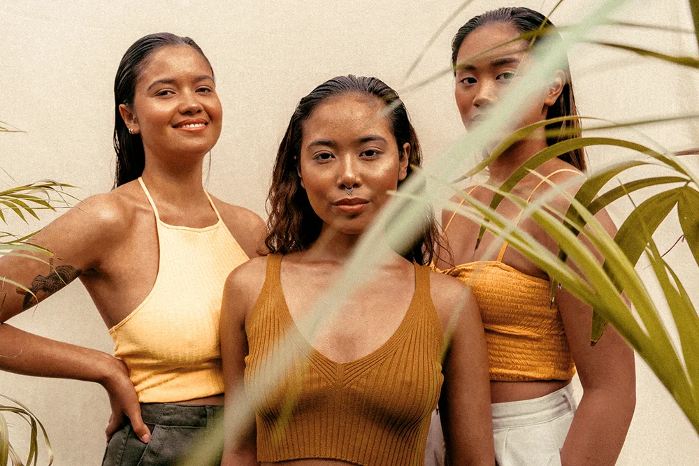 three women of ethnic minority backgrounds with coconut oil in their hair, standing in front of a beige background