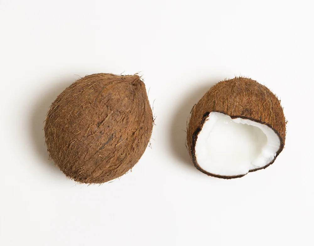 a whole brown coconut and half a coconut placed together on a white surface