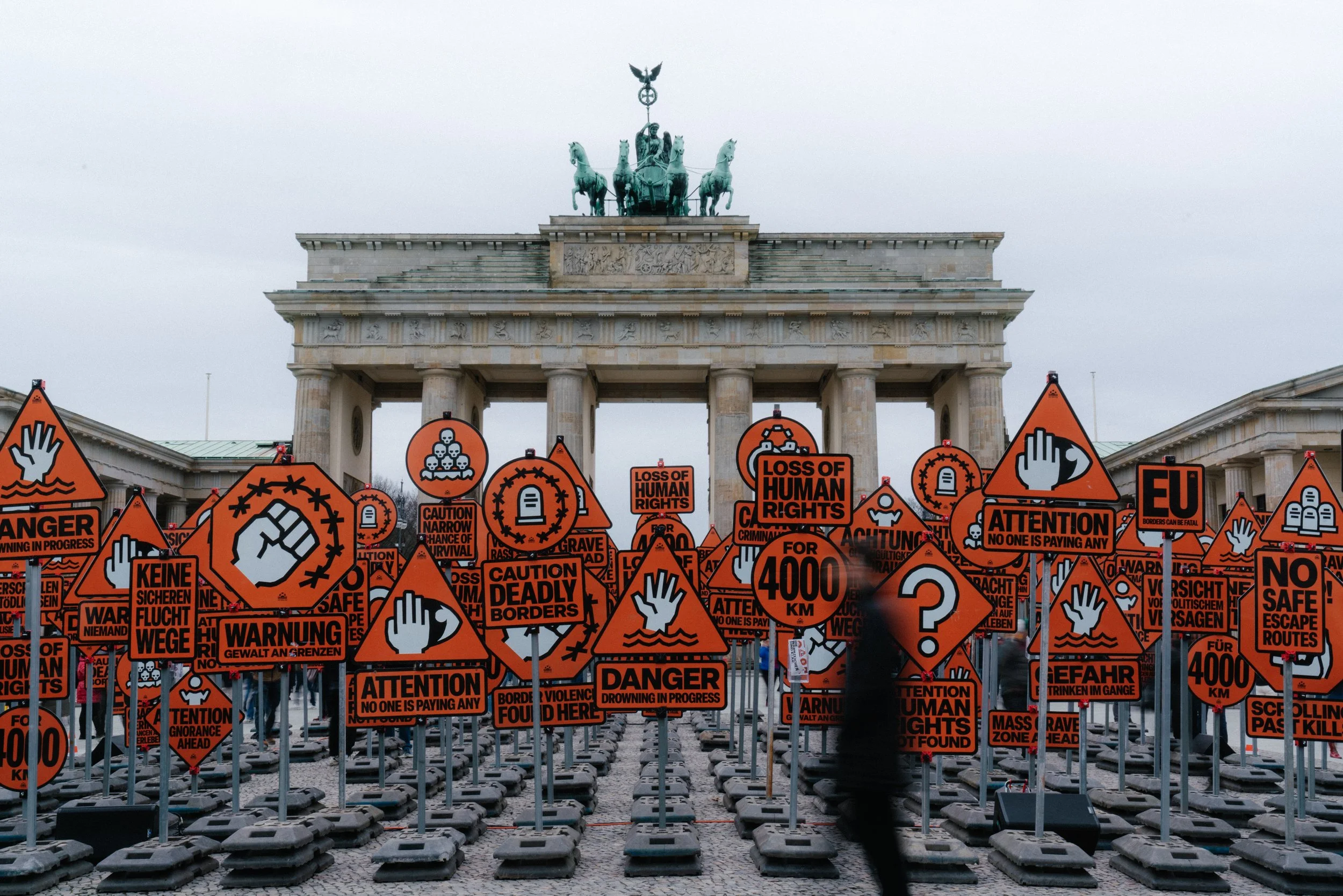 Protest with numerous orange warning signs and symbols in front of the Brandenburg Gate in Berlin, Germany.