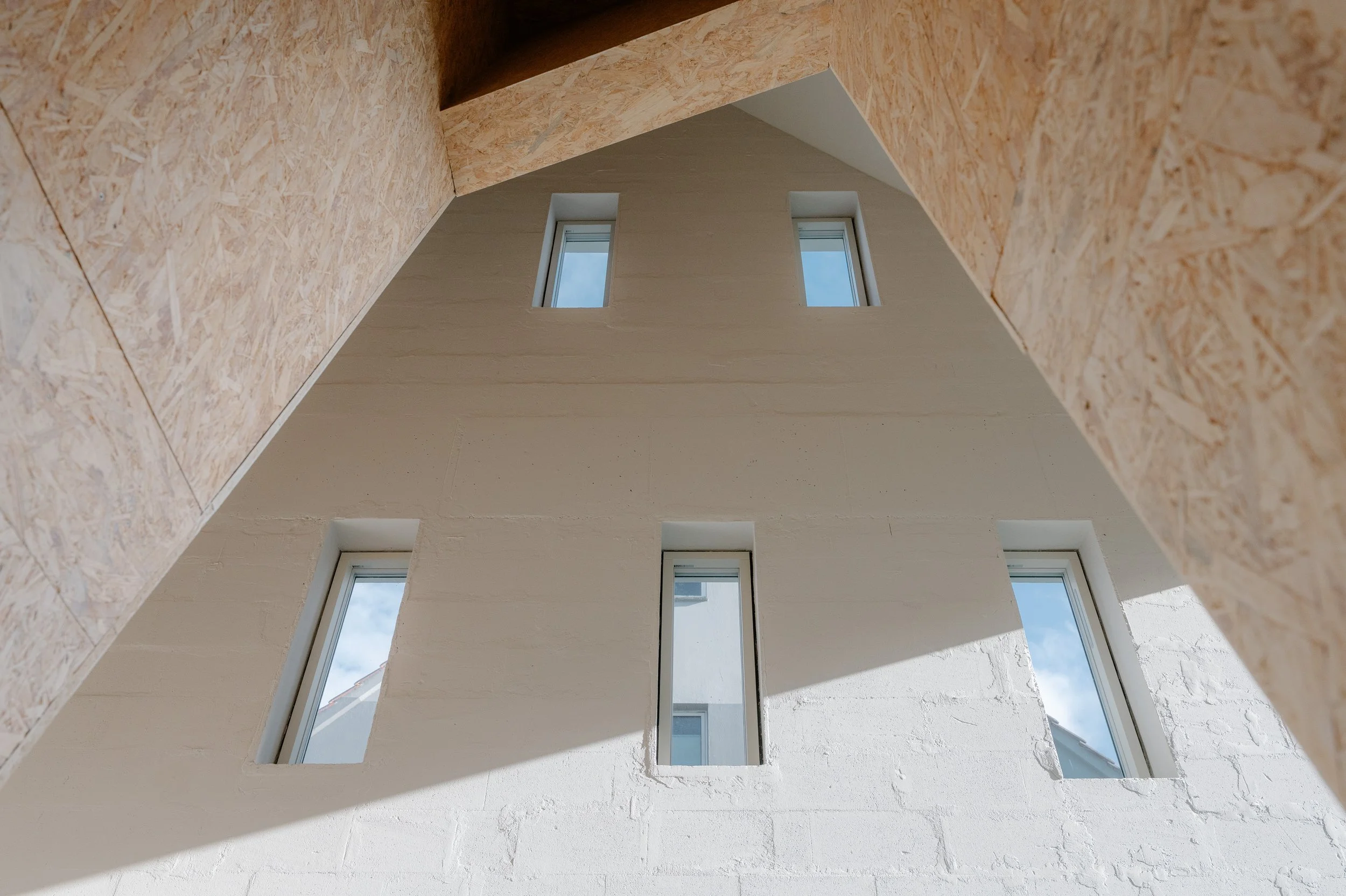 Interior view looking up at a multi-story white building with five rectangular windows, with sunlight creating a shadow on the wall.