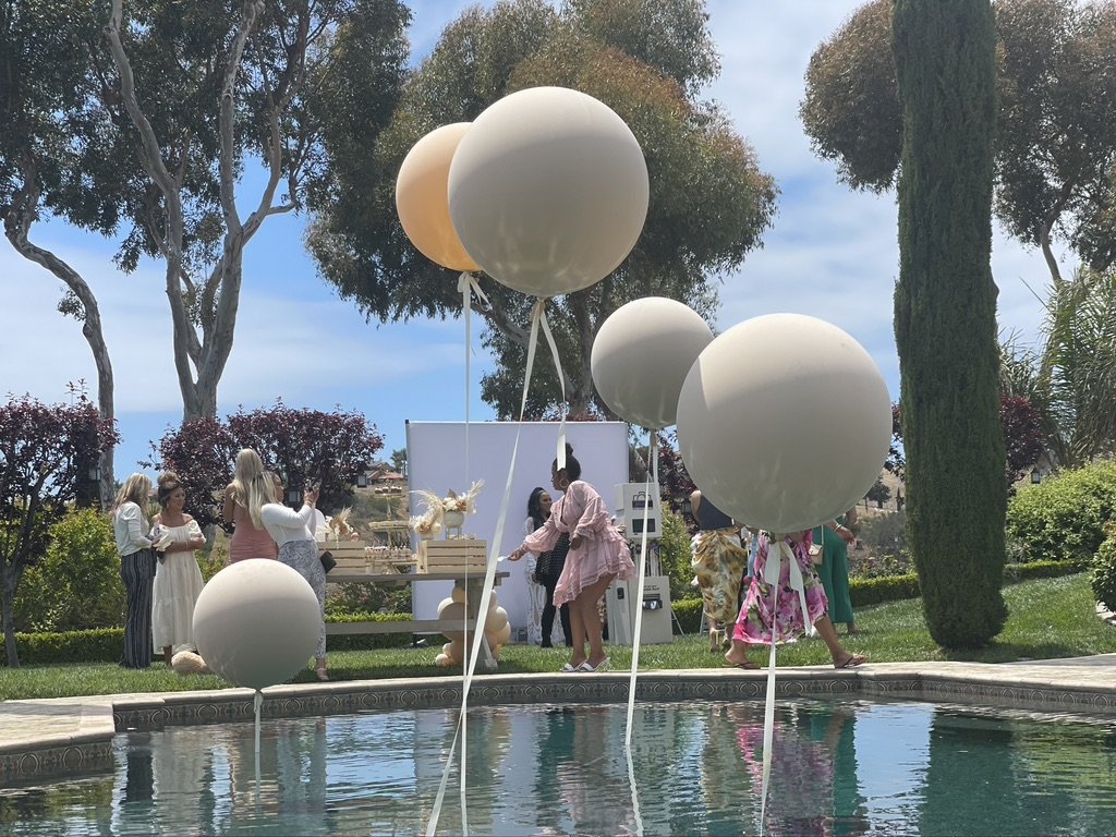 People celebrating with large white and beige balloons near a swimming pool outdoors during daytime.