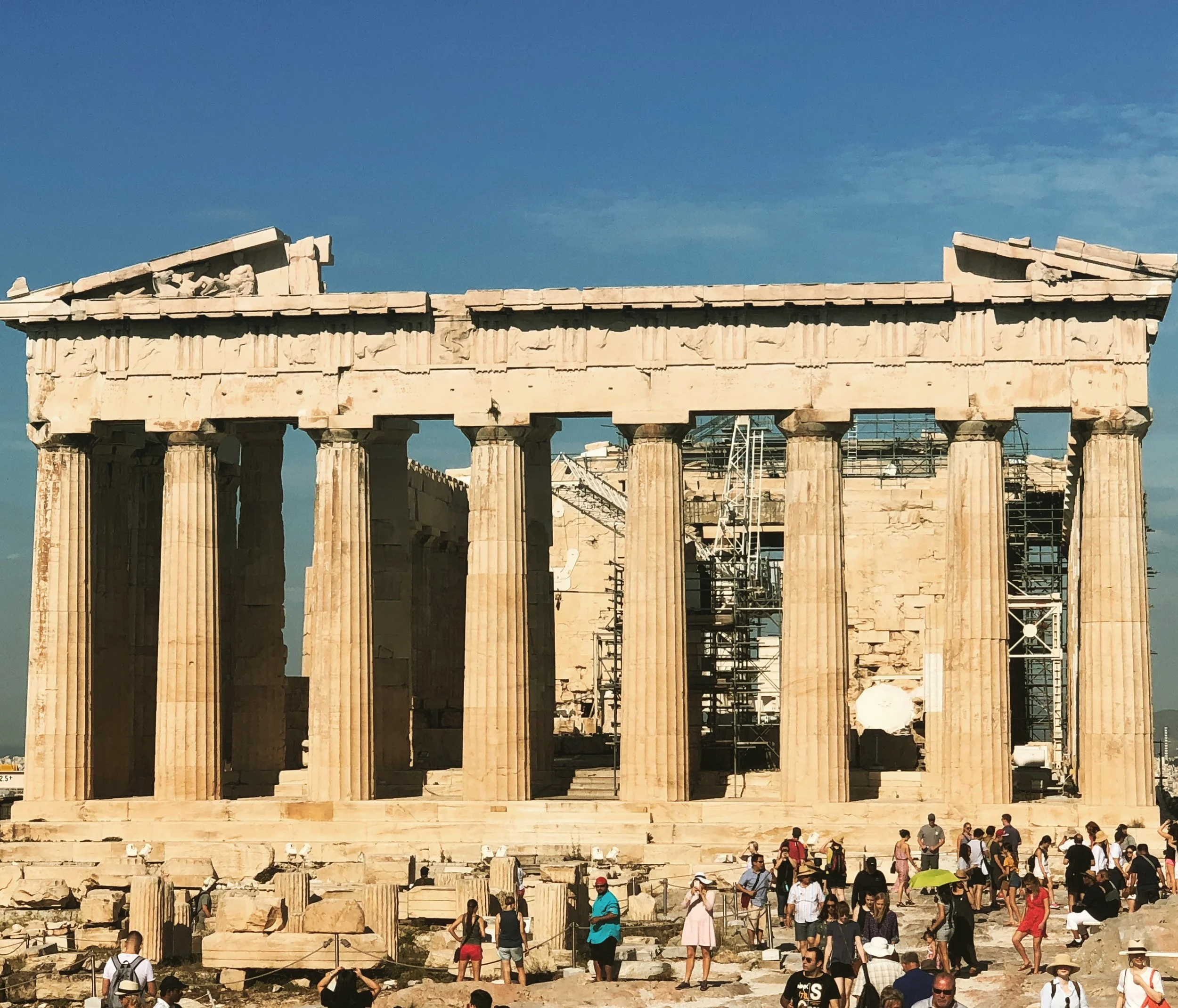 The Parthenon in Athens, Greece, with tourists in front, under clear blue sky.