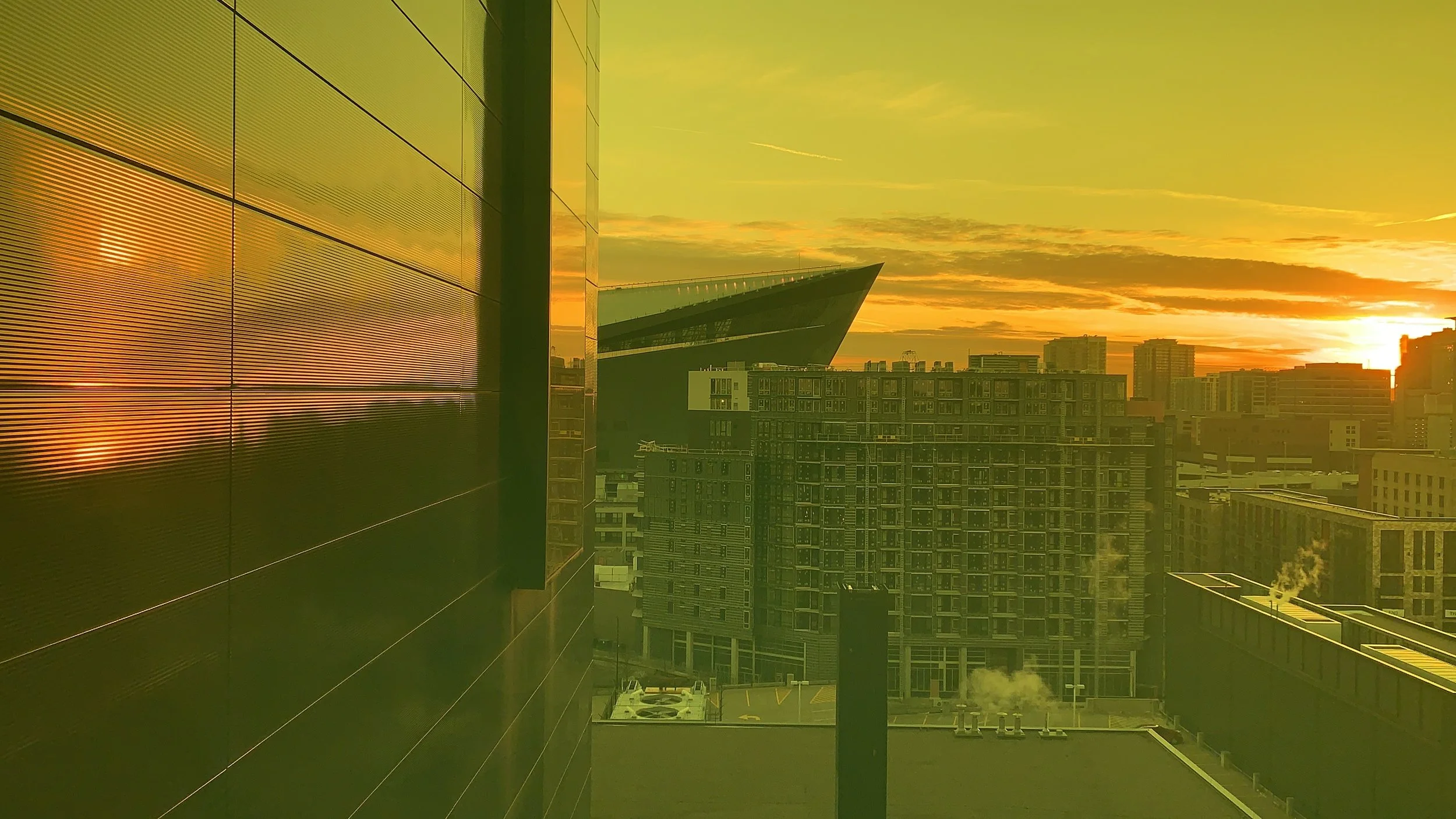 Cityscape at sunset with modern buildings and yellow-orange tinted sky.