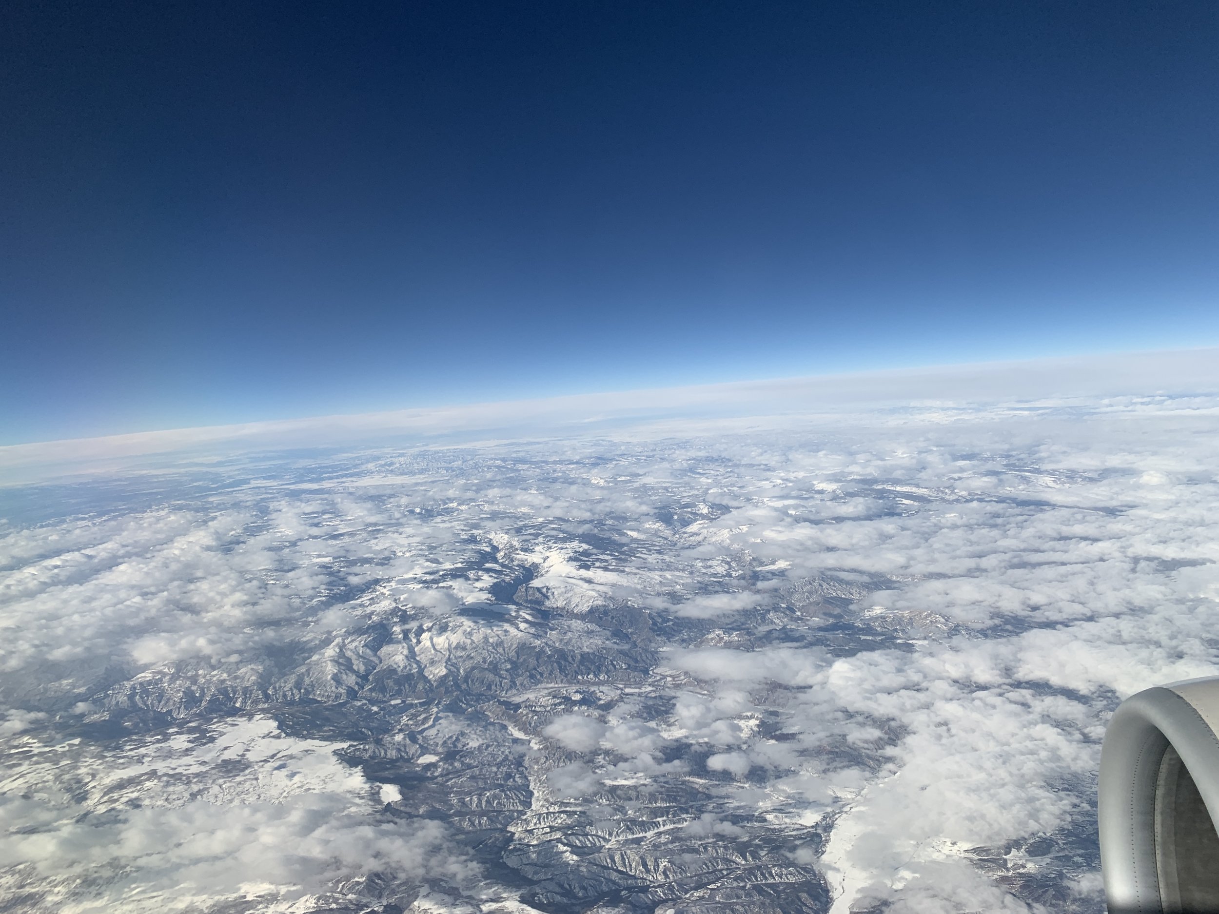 Aerial view of snow-covered mountains and clouds from an airplane window.