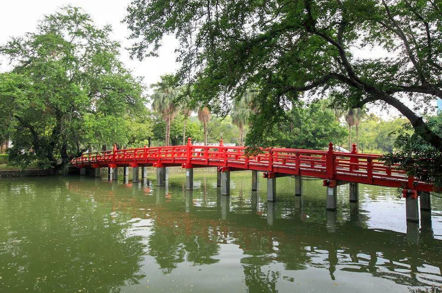 A red Japanese style wooden bridge over a lake in leafy Taichung Park, Taiwan.
