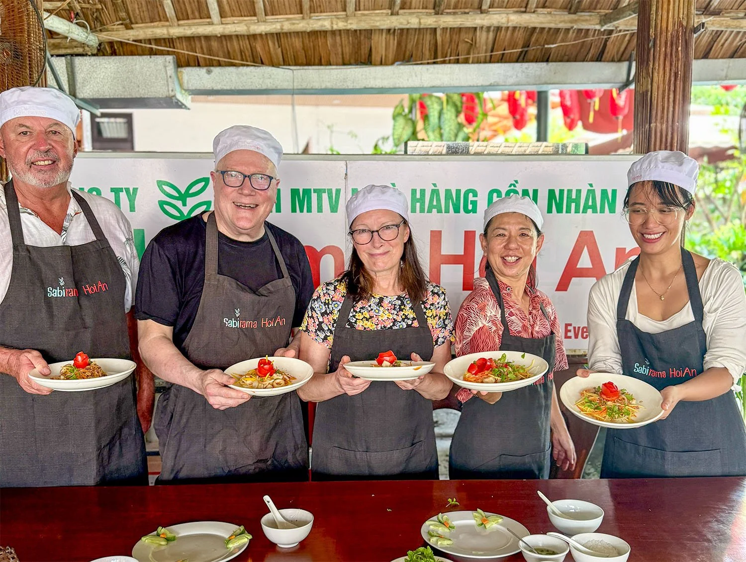 Four retirees show off the results of their cooking class in Hoi An, Vietnam, standig behind a table with their Vietnamese host.