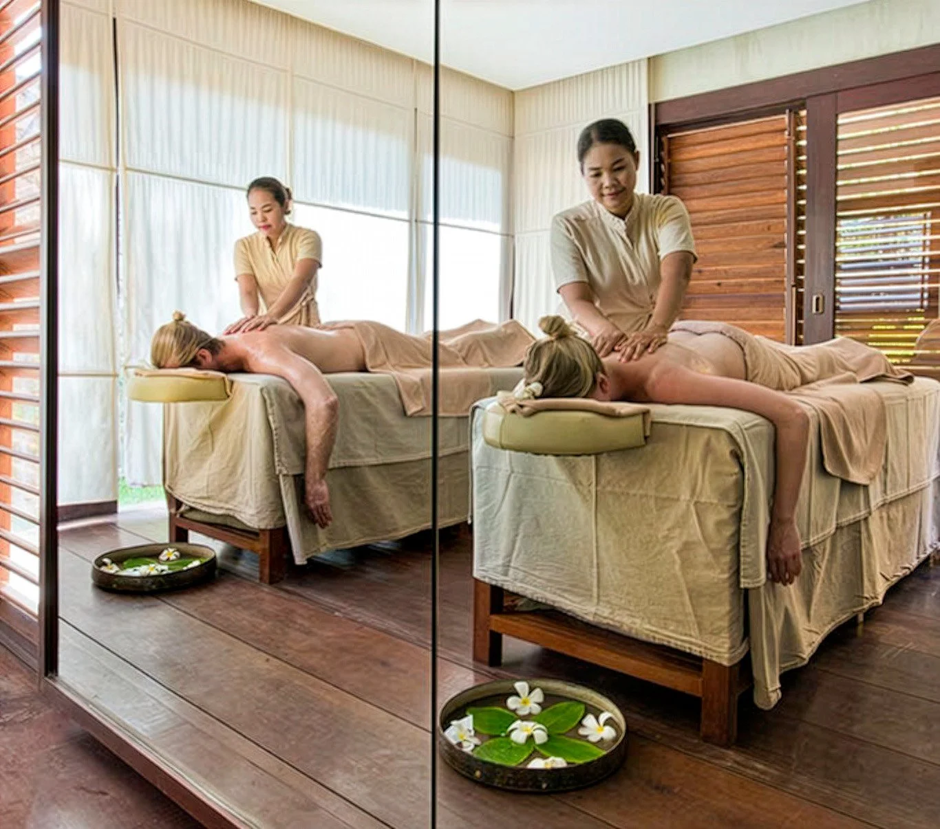 A reflection in a wall mirror of two female massage therapists giving back massages to two female clients.