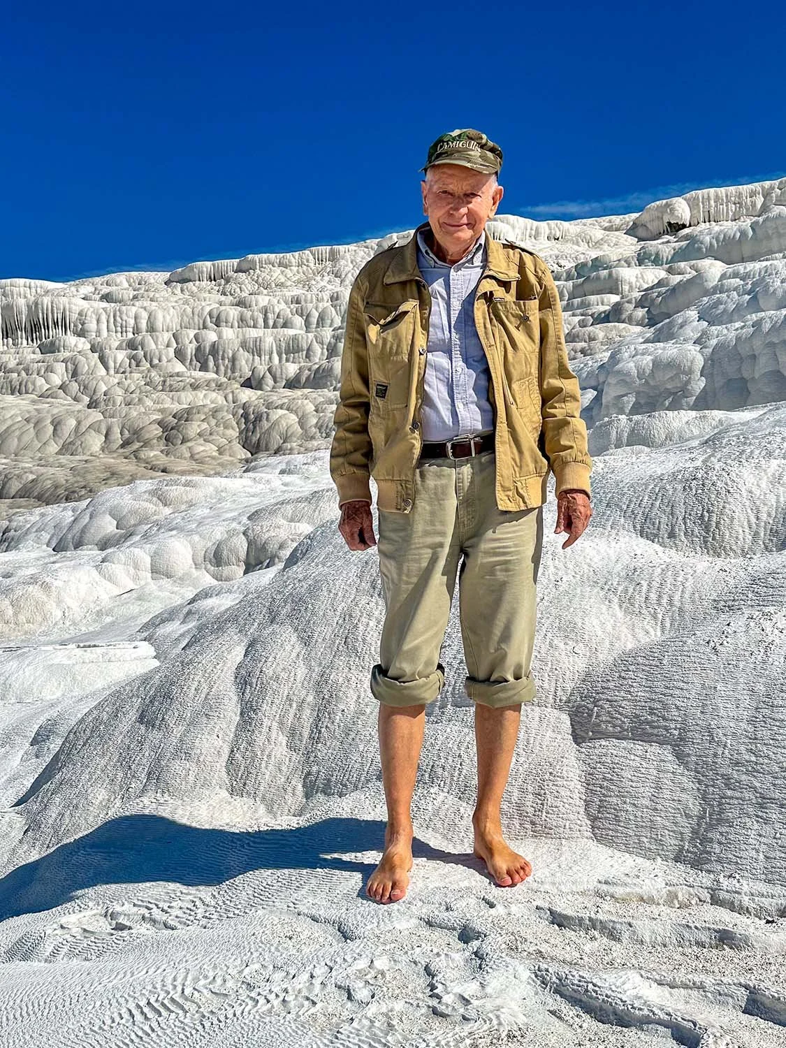 An elderly bare-footed man standing on the Pamukkale Travertine Terraces in Turkiye in bright sunshine.