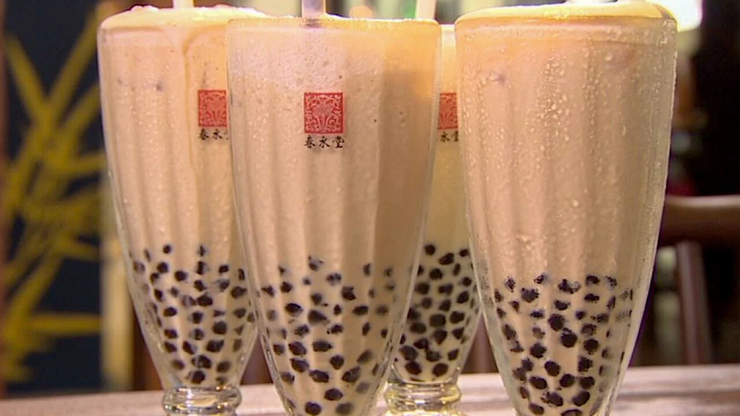 Close-up of four tall glasses of icy cold brown bubble tea with black tapioca pearls at the bottom on a table in Taichung, Taiwan.