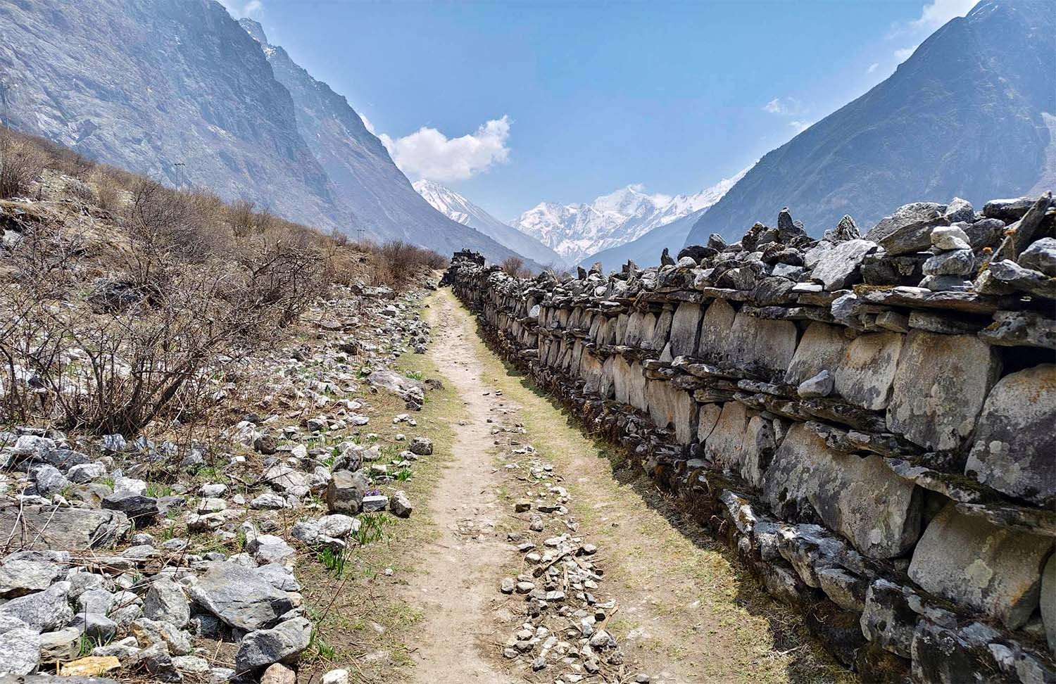 A walking trail follows a stone wall towards a valley in the high Himalayan mountains of Nepal..
