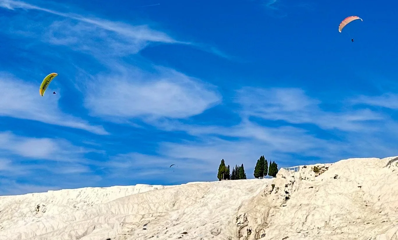 Two paragliders fly over the Pamukkale travertine terraces in Türkiye.