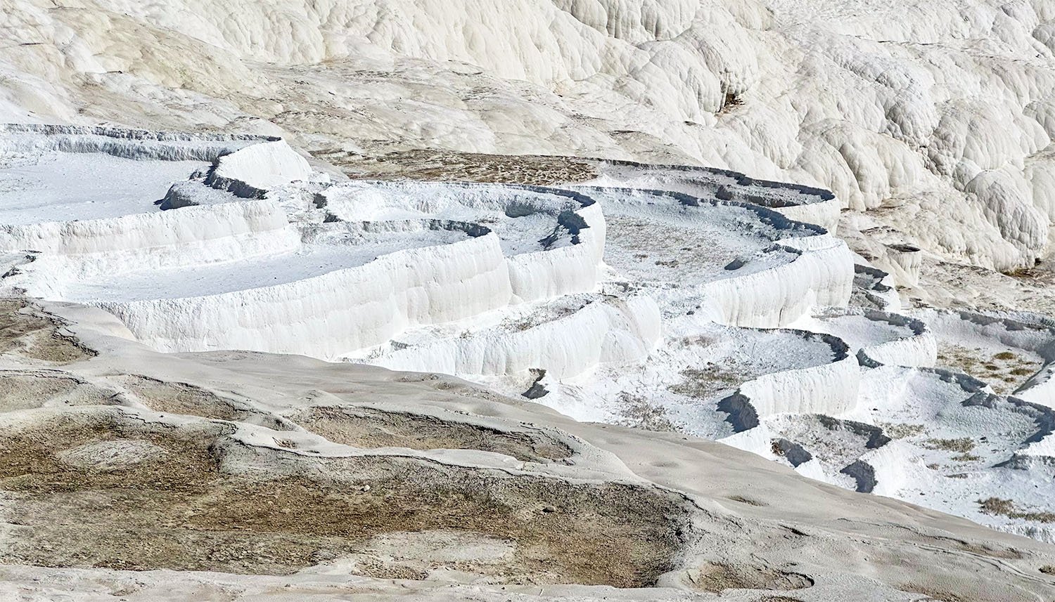 View across dry limestone pools on the travertine terraces at Pamukkale, Türkiye.