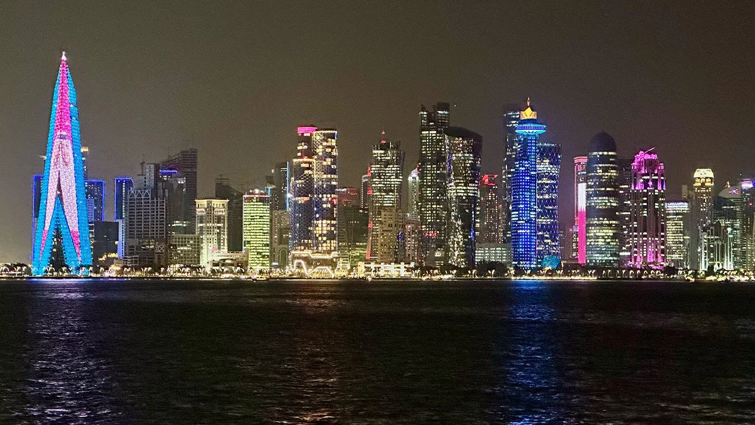 Nighttime view across Doha Bay to West Bay from Al Corniche, Doha, Qatar, with brightly lit skyscrapers on the West Bay shoreline..