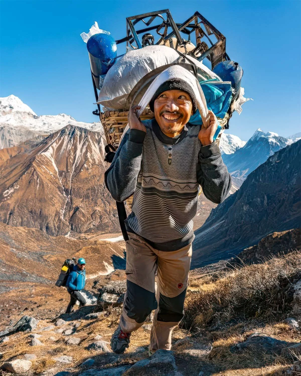 A mountain porter carrying a traditional load along a rugged trail in the Himalayan Mountains of Nepal.