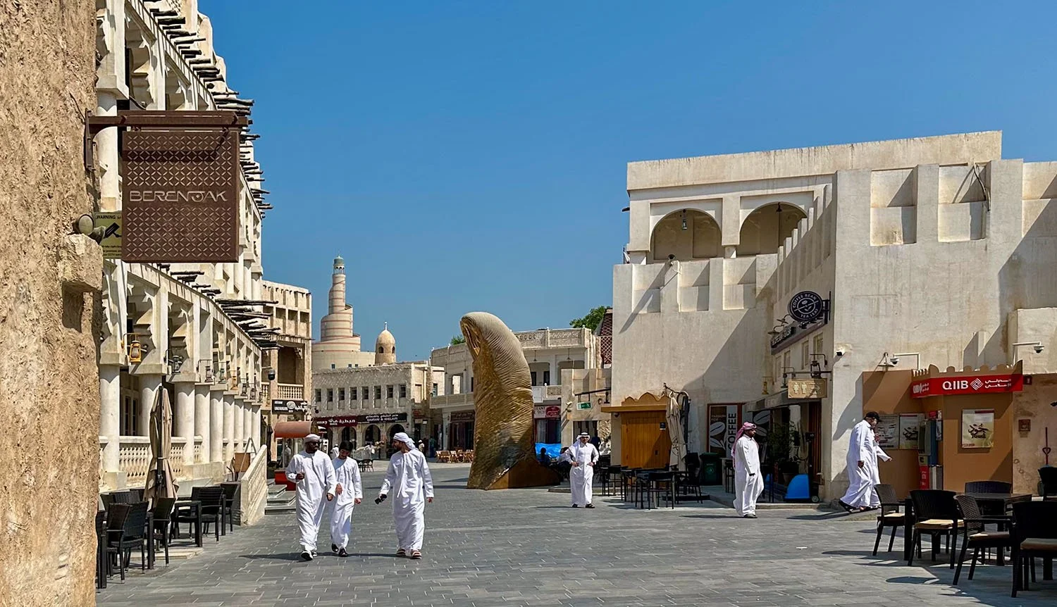 Wide view of a street inside Souq Waqif in Doha, Qatar, with men wearinf thobes and ghutras walking towards the camera.