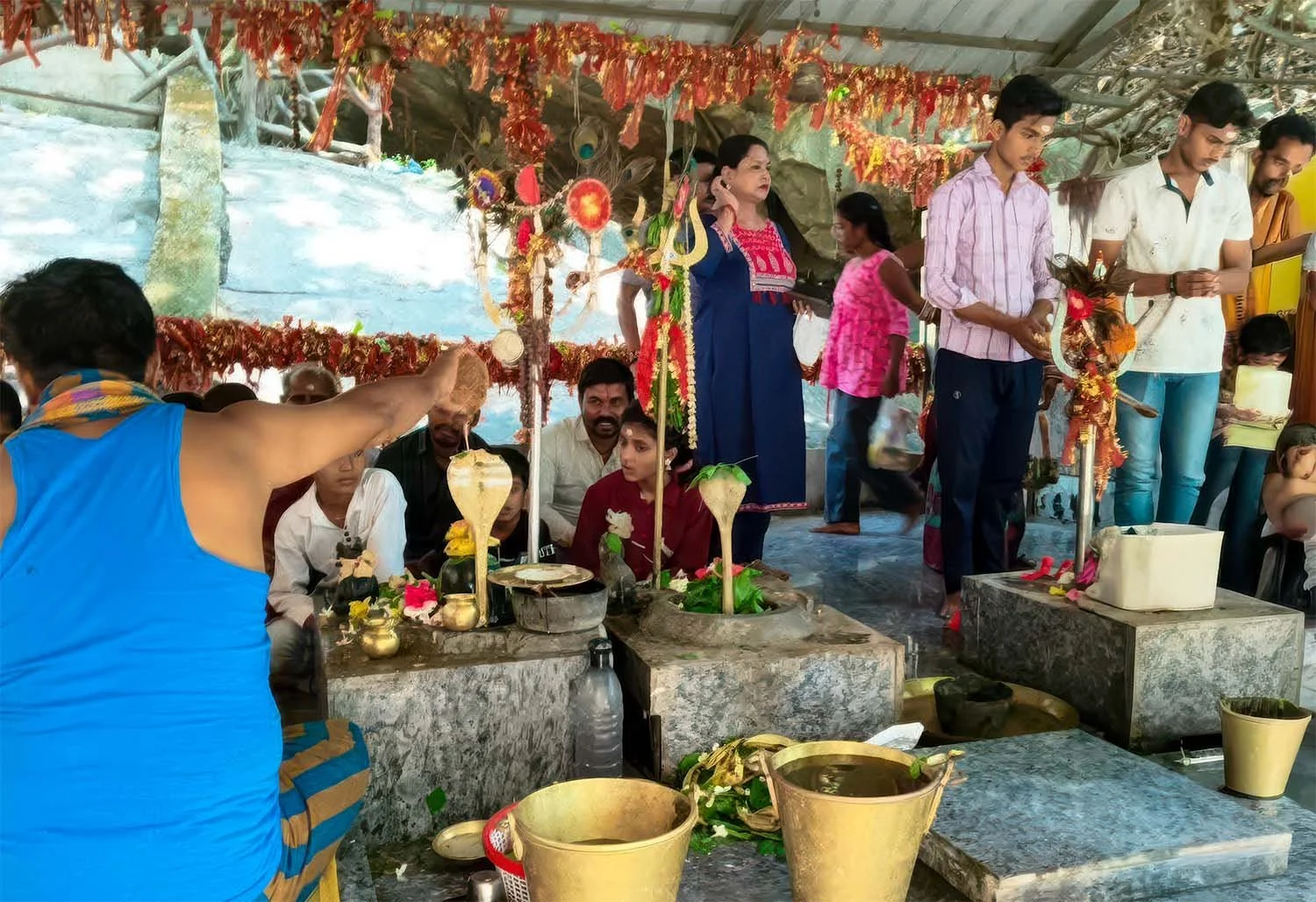 A priest and devotees gathered around the stone lingams during a ritual at the Panchalingeswar Shrine, Odisha, India.