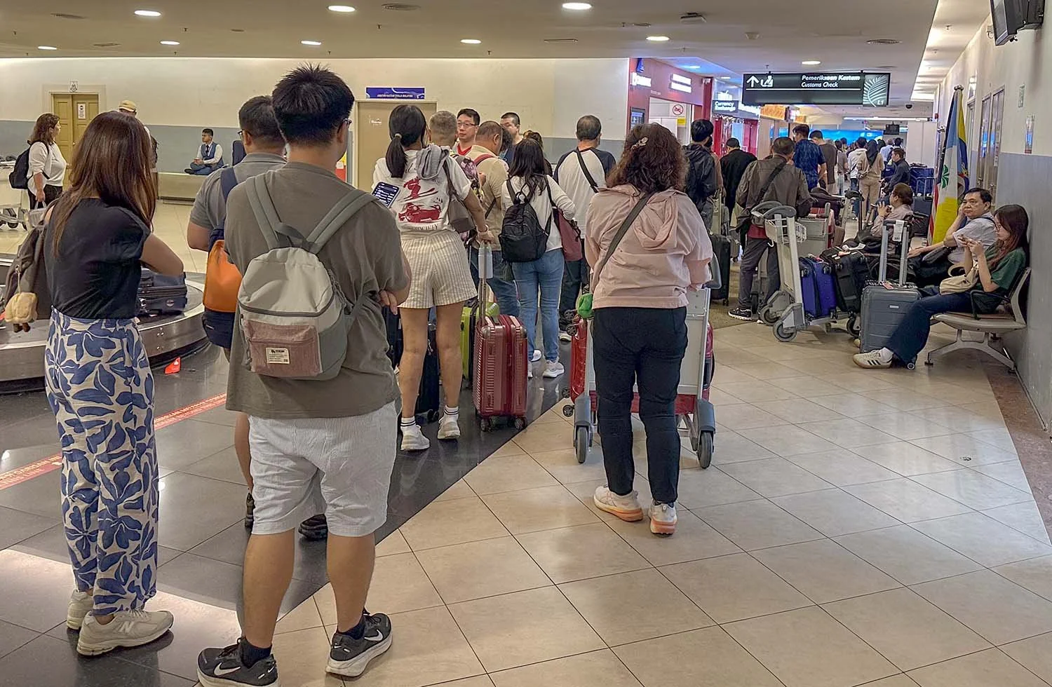 Airline passengers with baggage queuing for customs inspection at Penang International Airport.